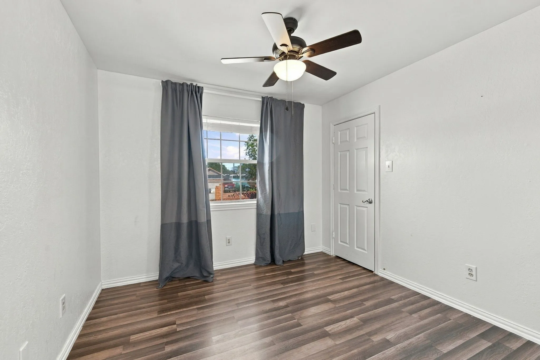 Wood-finish flooring, white walls, ceiling fan with integrated lighting, and a white paneled door