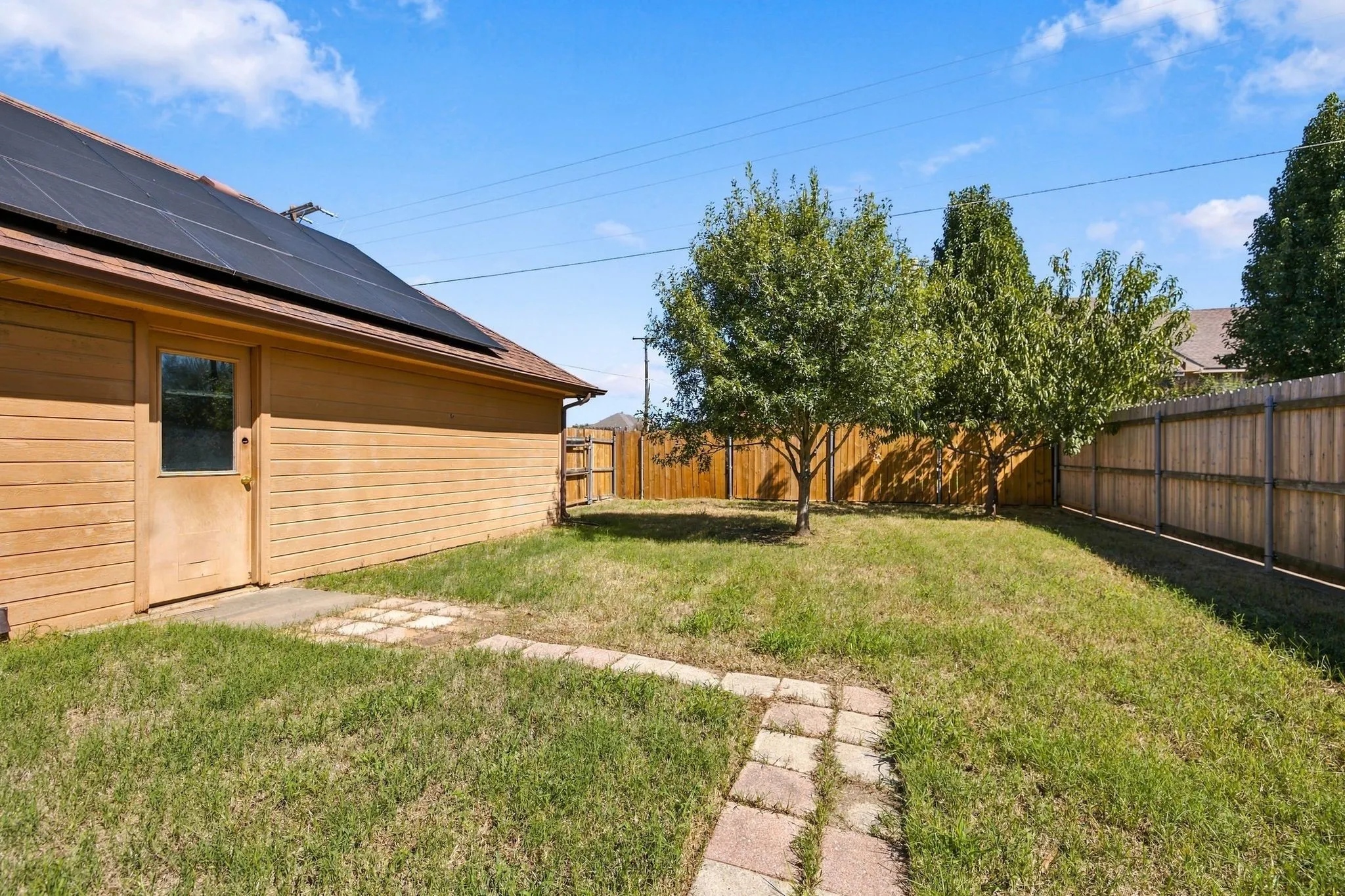 Side yard featuring a stone paver pathway, mature trees, and a wood privacy fence