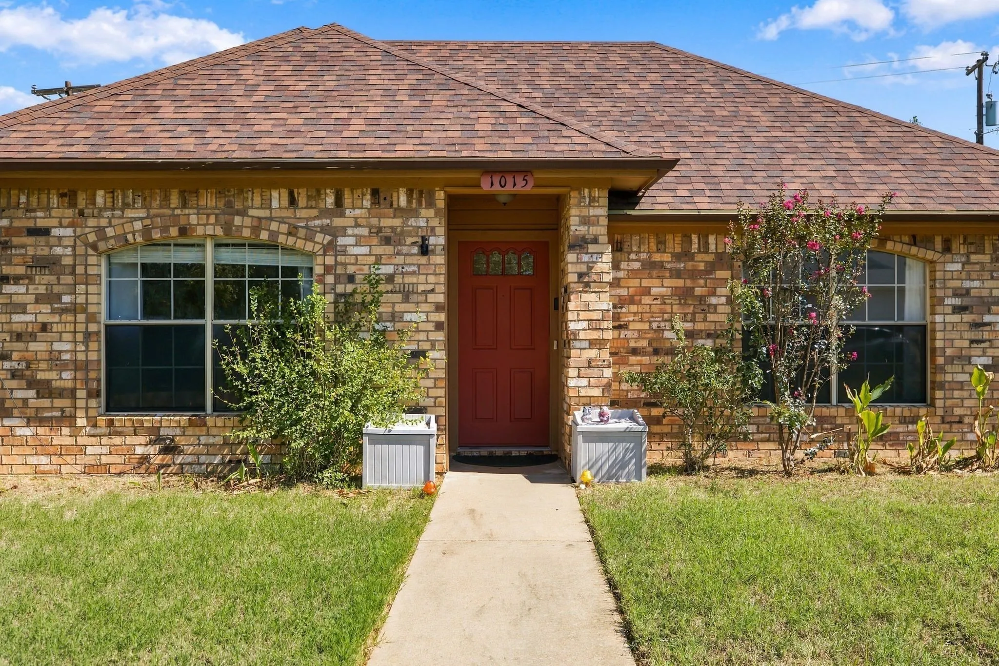 Brick exterior with arched window detailing, a red entry door with decorative glass, and a brown shingle roof