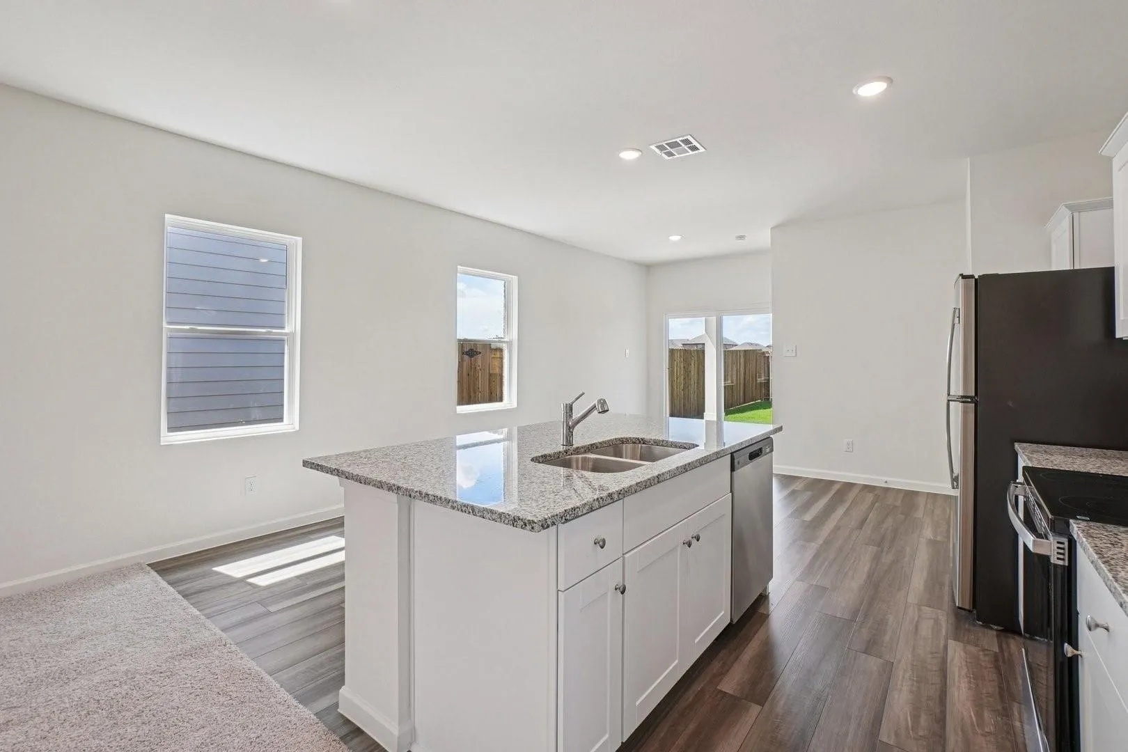 Kitchen island with a double basin sink, stainless steel appliances, white cabinetry, granite countertops, and wood-finish flooring