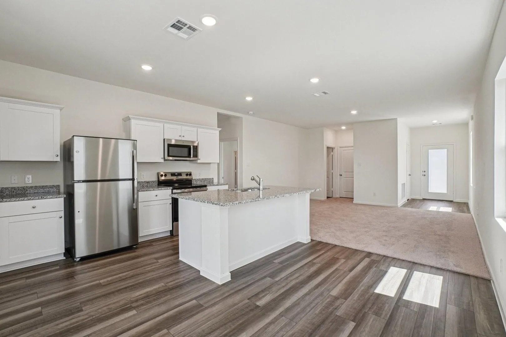 Open-concept living space featuring a kitchen island with a built-in sink, stainless steel appliances, white cabinetry, and granite countertops