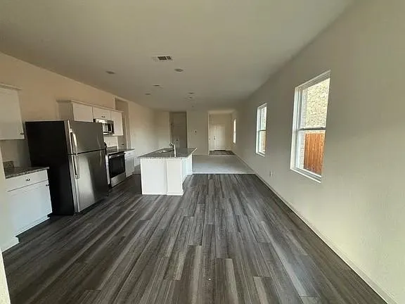 Spacious open-concept layout with wood-finish flooring, white cabinetry, granite-style countertops, and stainless steel appliances