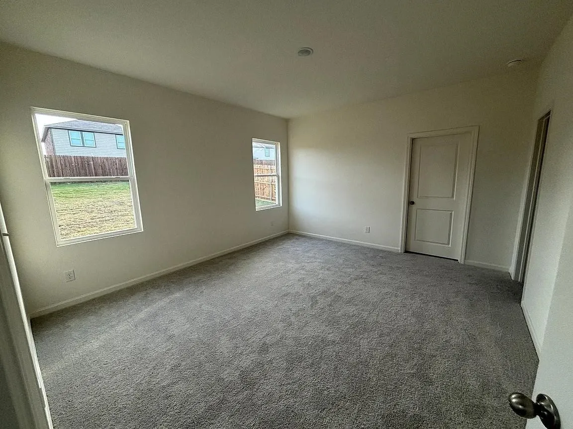 Plush grey carpeting, two rectangular windows, and a panel door with dark hardware