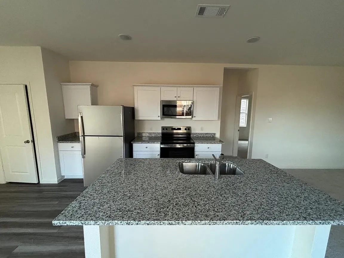 Kitchen featuring an island with a dual basin sink, stone-finish countertops, white cabinetry, wood-finish flooring, and stainless steel appliances