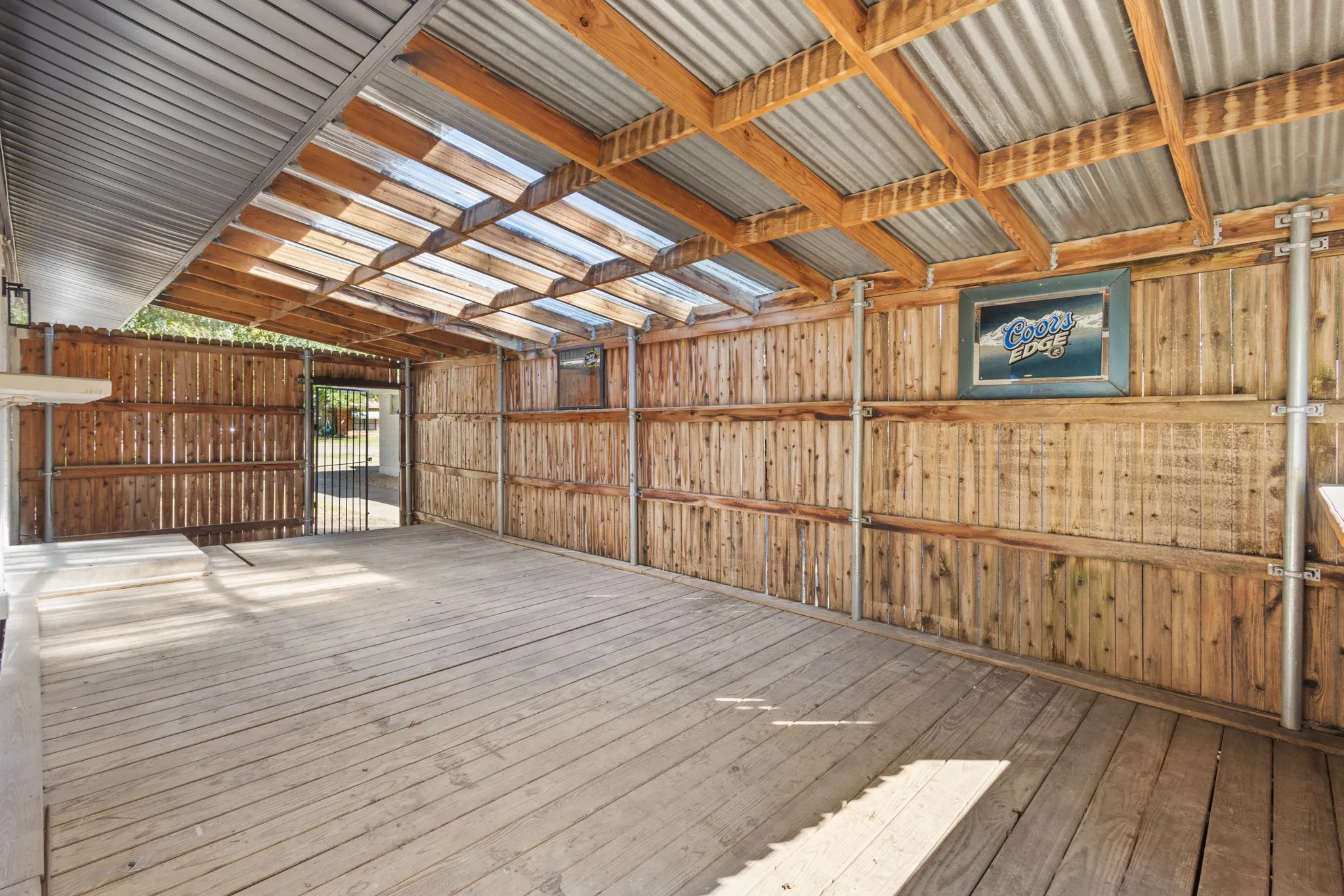 Expansive covered outdoor area featuring wood decking, a corrugated metal and clear panel roof, and natural wood plank walls, excellent for outdoor dining and activities