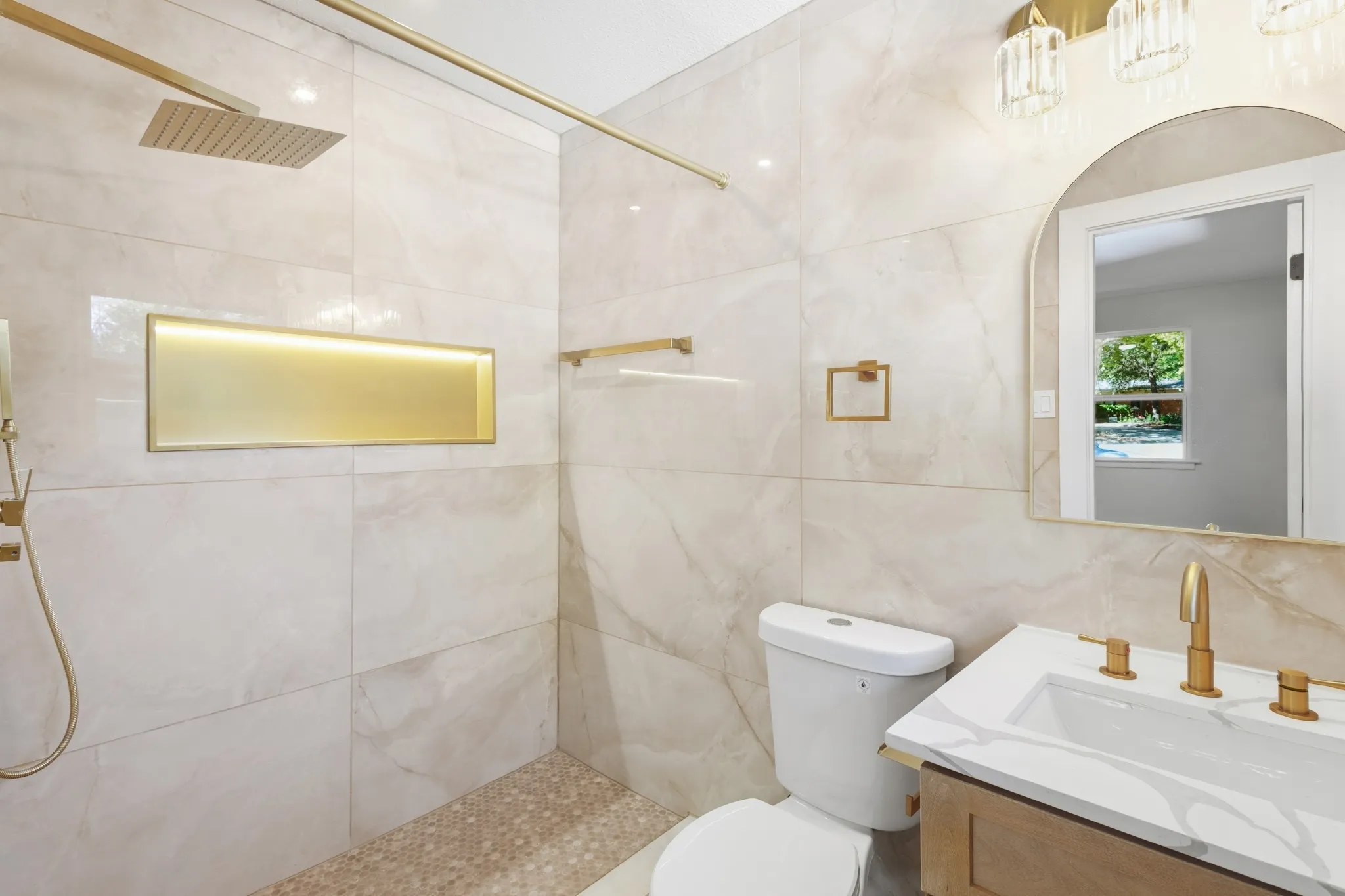master bathroom featuring wall to wall tile shower with a gold-toned niche, a rain shower head, and a pebble-tiled floor