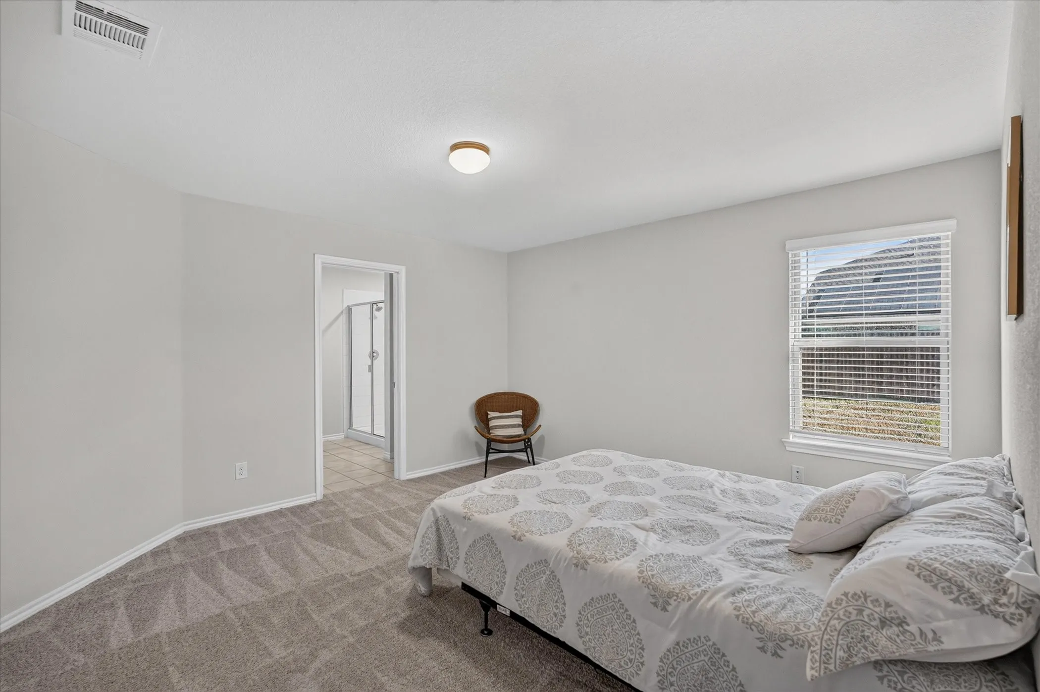 Spacious bedroom featuring neutral wall finishes, abundant natural light from a large window with blinds, wood-finish flooring with carpet inlay, and a ceiling-mounted light fixture