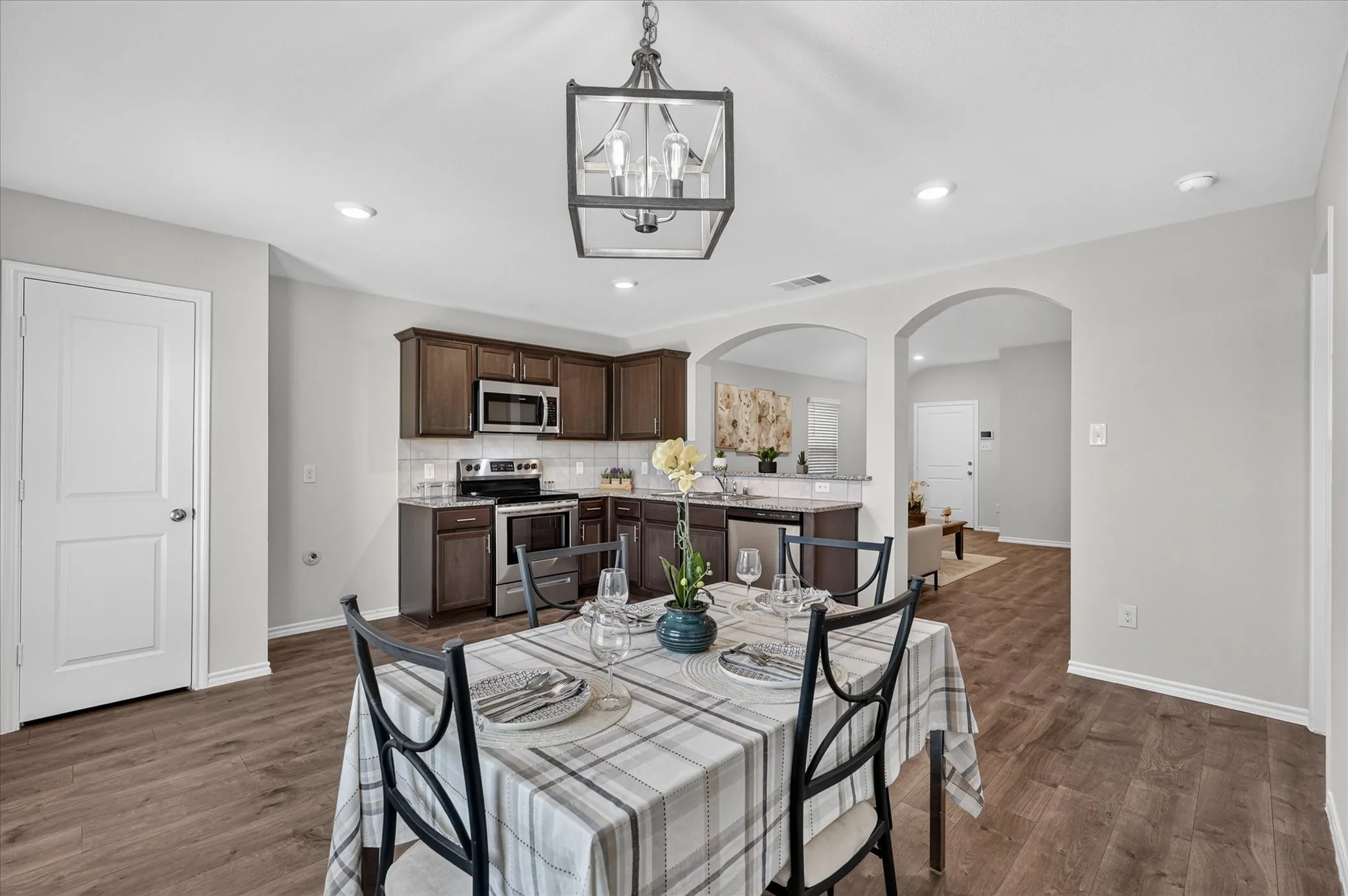 Open-concept kitchen and dining area featuring wood-finish flooring, dark wood cabinetry, stainless steel appliances, and a white subway tile backsplash