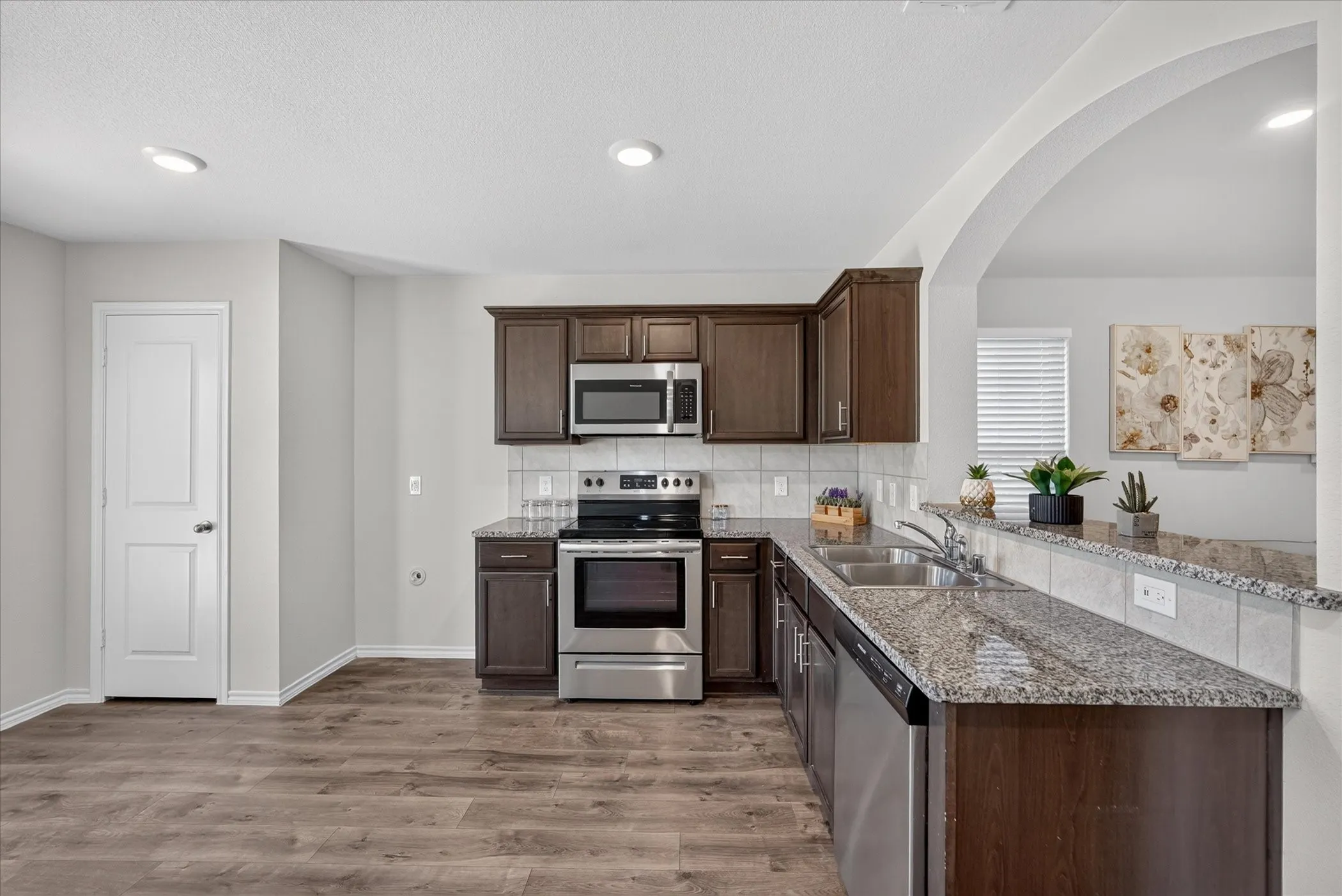 Wood-finish flooring, dark wood cabinetry, stainless steel appliances, granite countertops, and a subway tile backsplash