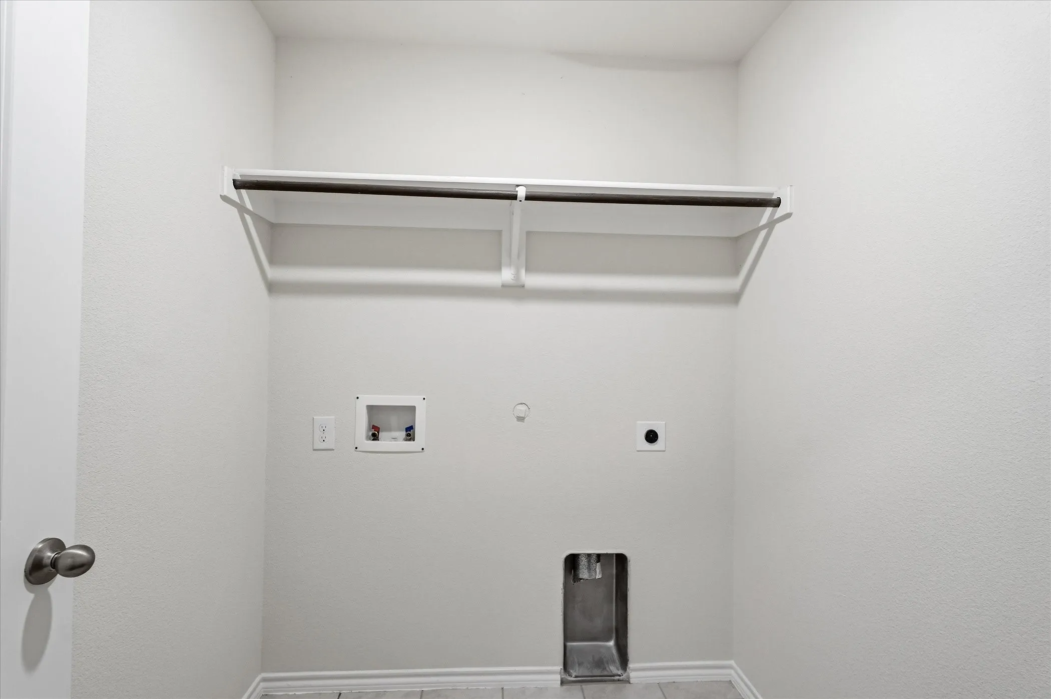 Utility room with a built-in shelving unit and clothing rod, featuring dedicated appliance hookups and neutral wall finishes