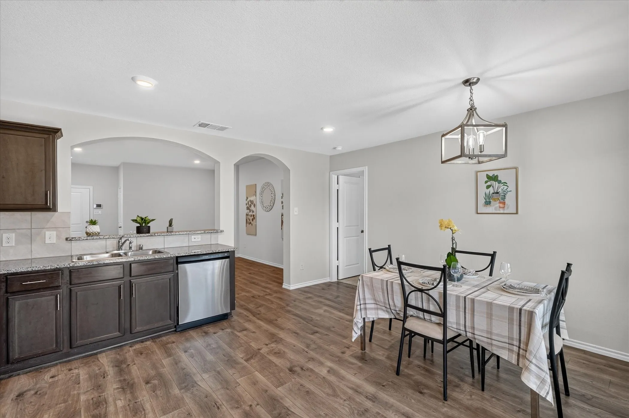 Wood-finish flooring throughout, dark wood-finish cabinetry, granite-style countertops, stainless-steel dishwasher, and recessed lighting