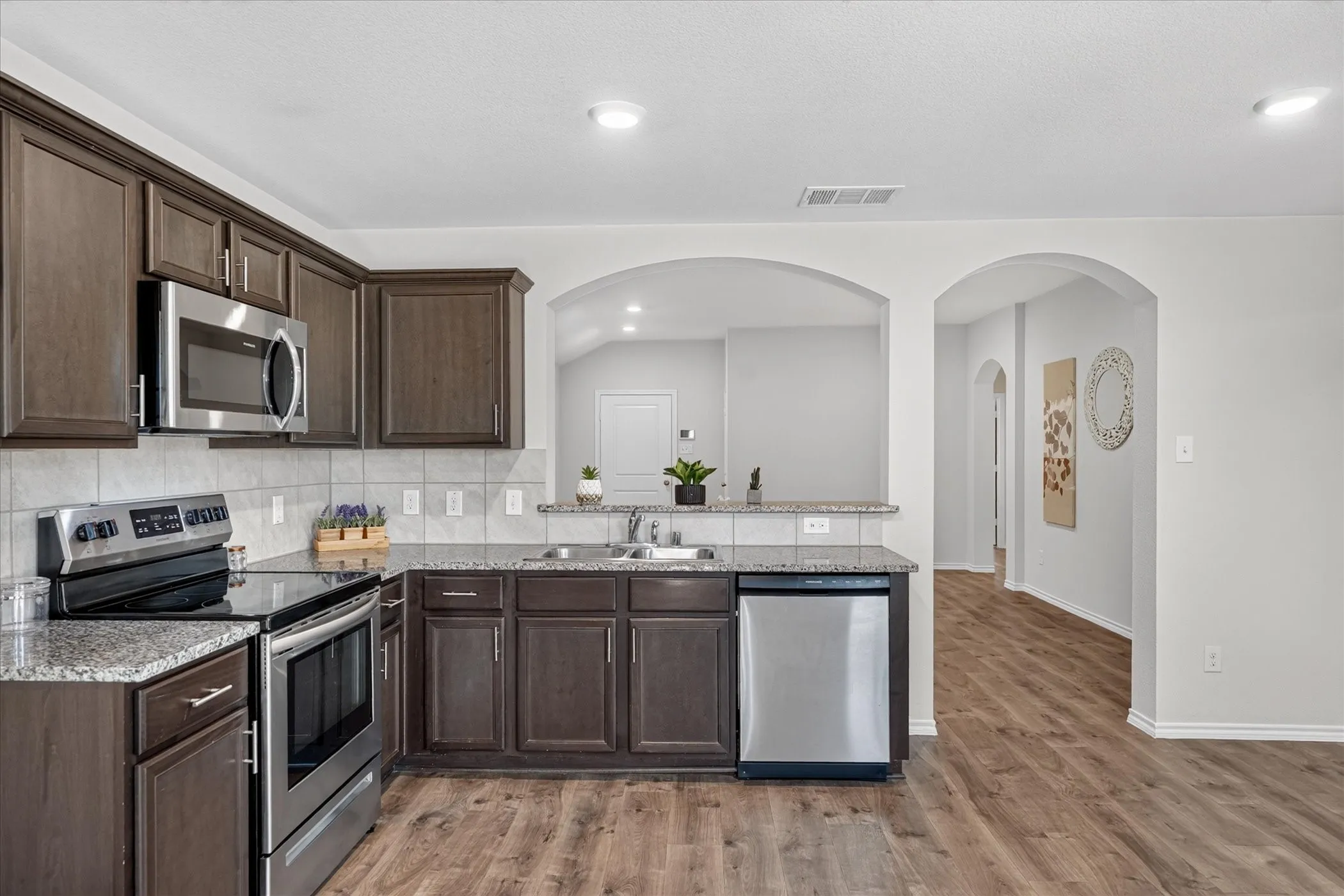 Kitchen featuring dark wood-finish cabinetry, stainless steel appliances, granite countertops, and a tile backsplash
