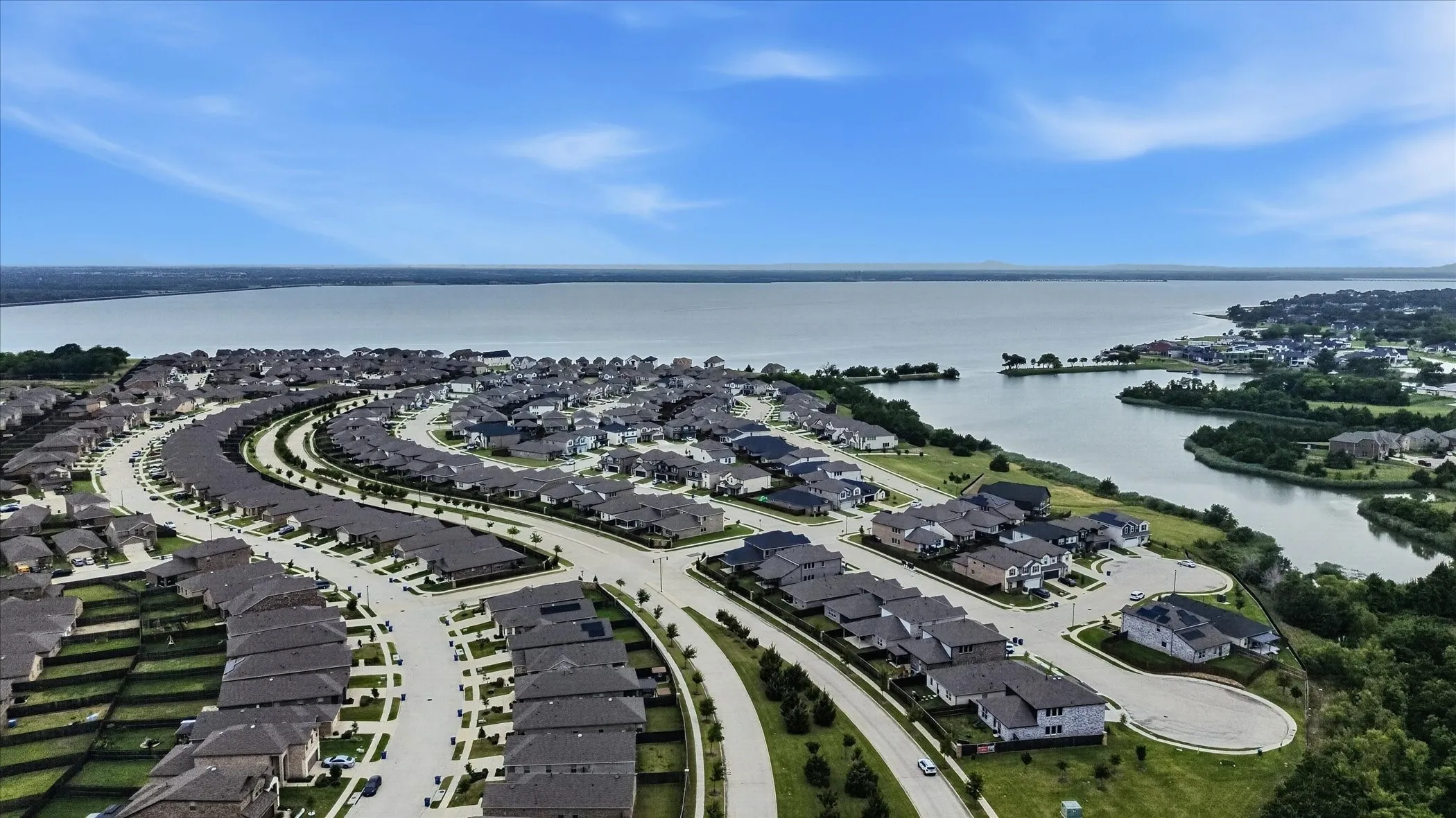 Residential development with curved streets and uniform roofing, bordered by a large body of water and natural landscaping