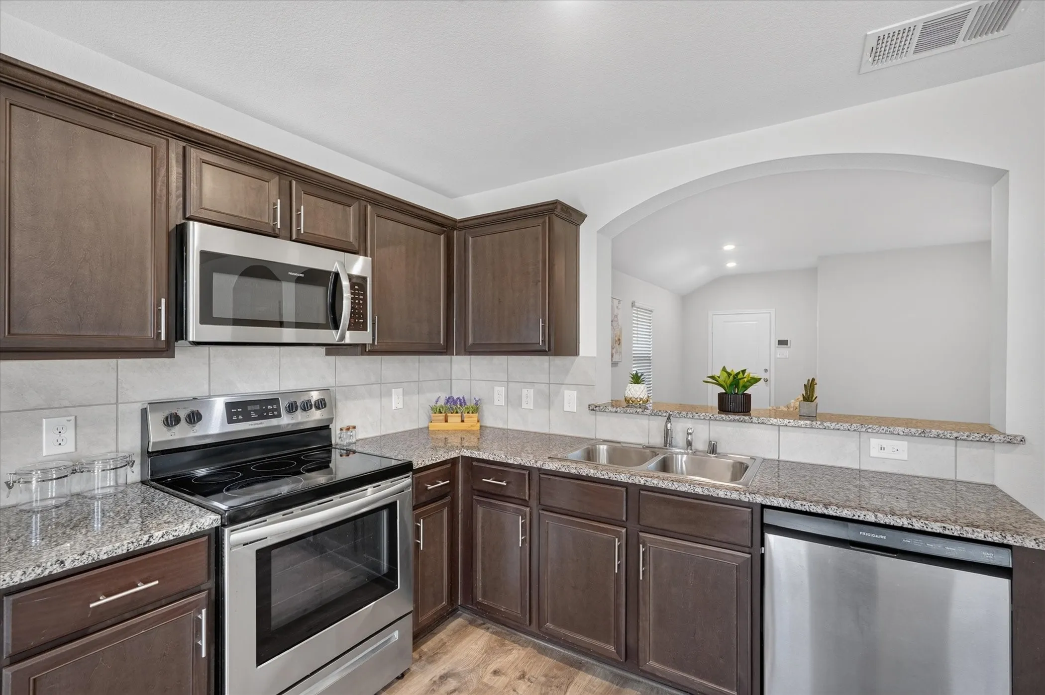 Kitchen featuring dark wood-finish cabinetry, stainless steel appliances, speckled stone countertops, and a tile backsplash