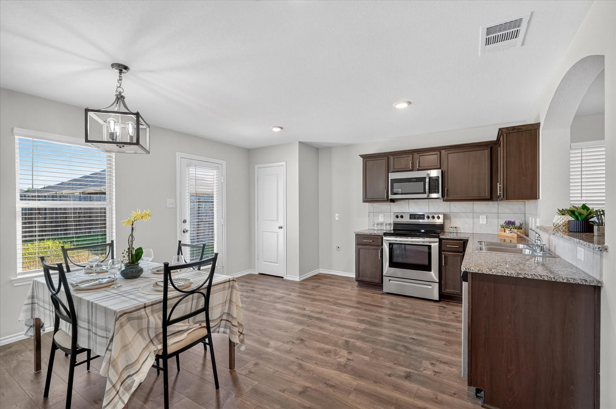 Spacious kitchen and dining area featuring wood-finish flooring, stainless steel appliances, dark wood cabinetry, and light-toned countertops
