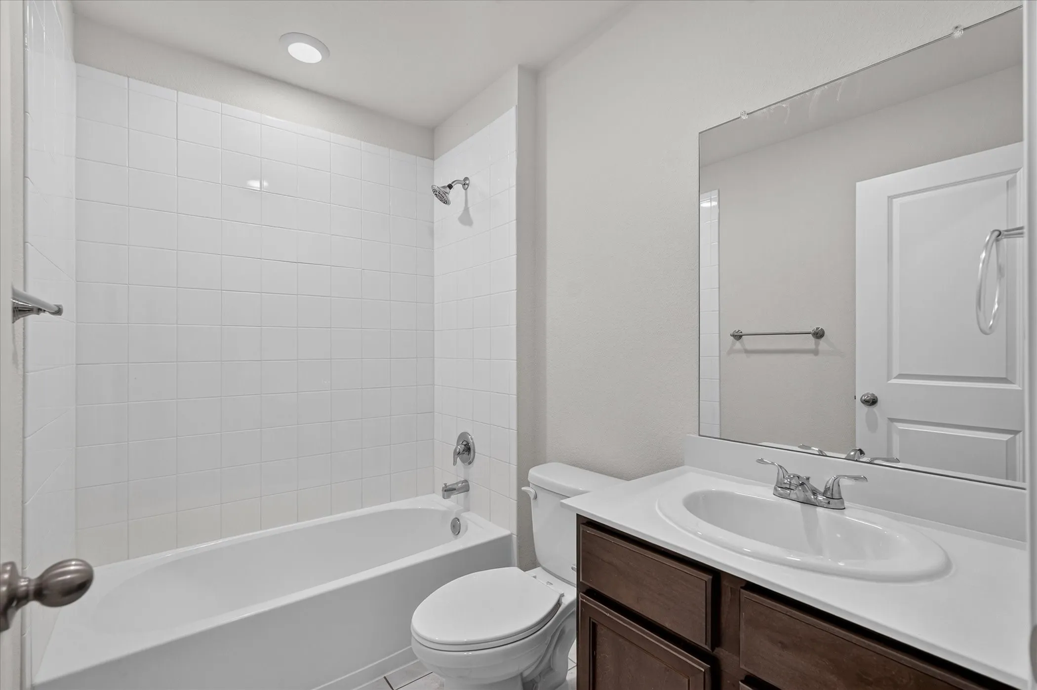 Bathroom featuring a white subway tile tub surround, recessed lighting, chrome fixtures, a wood-finish vanity, and a large wall-mounted mirror