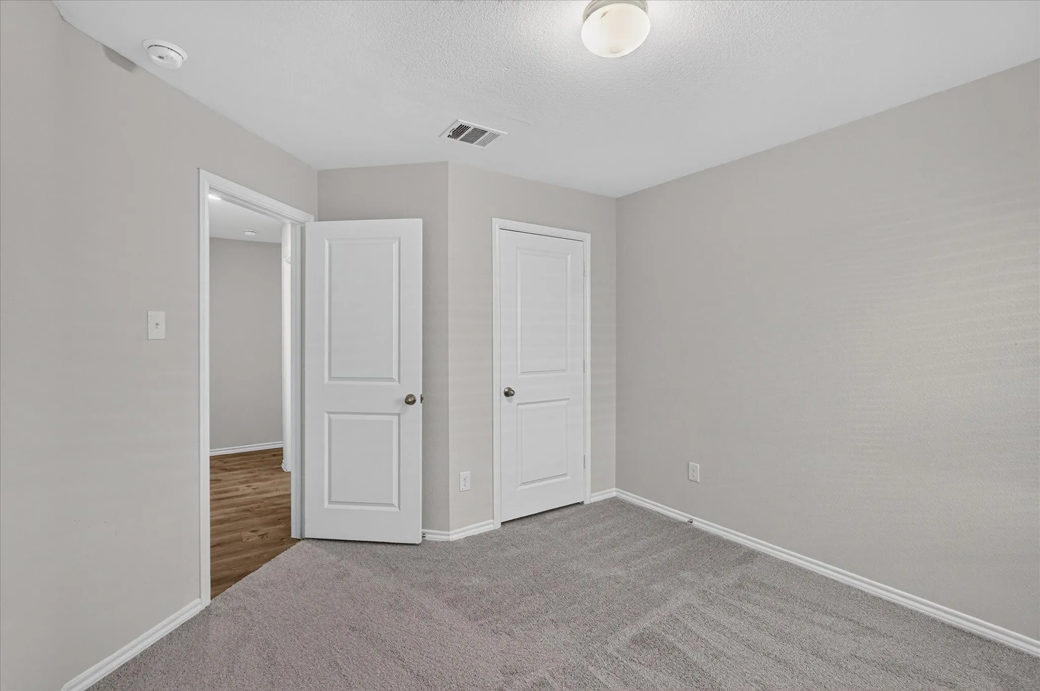 Light gray wall paint, textured ceiling, flush mount ceiling light fixture, white trim, and gray carpet flooring