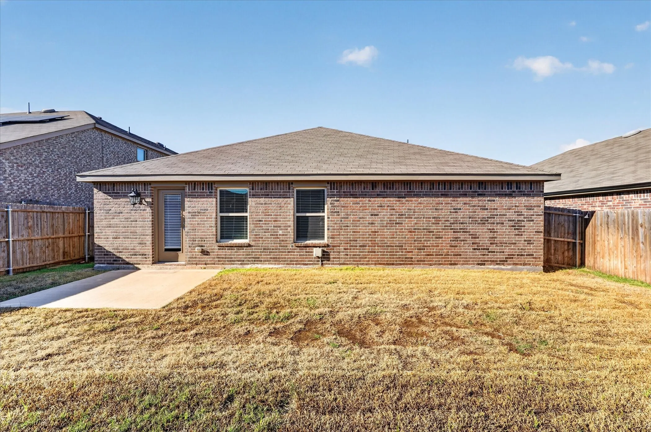 Brick single-story home featuring a hipped roof, multiple windows with dark frames, and a covered front entry