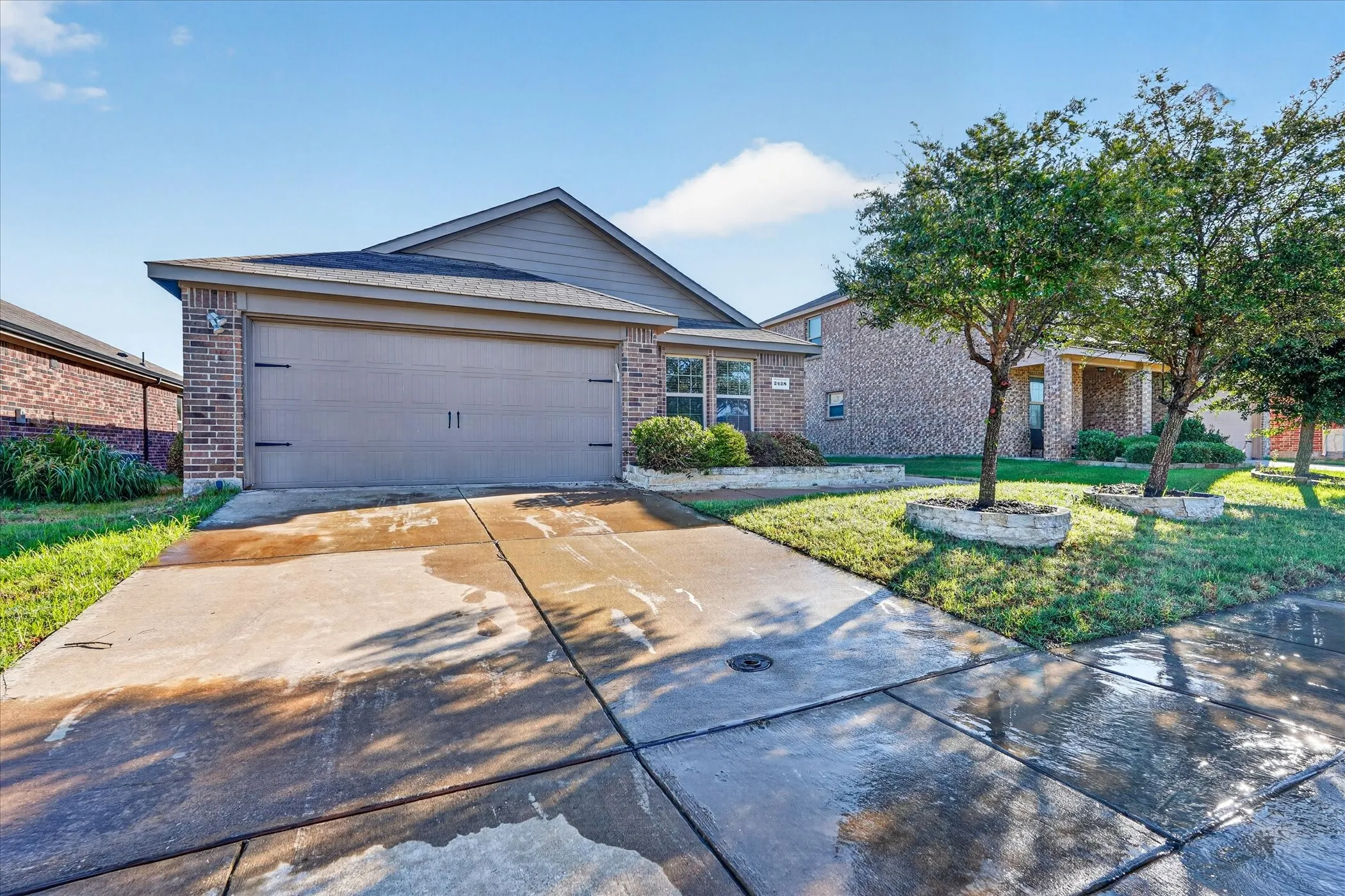 Brick veneer exterior with a two-car garage, concrete driveway, and established landscaping with stone-edged planters