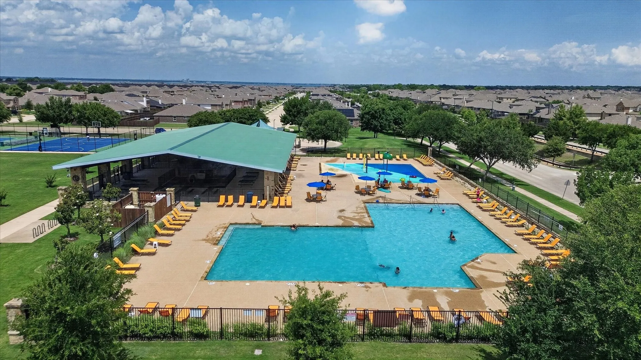Expansive community recreational area featuring multiple swimming pools, a covered pavilion, sports courts, and manicured green spaces