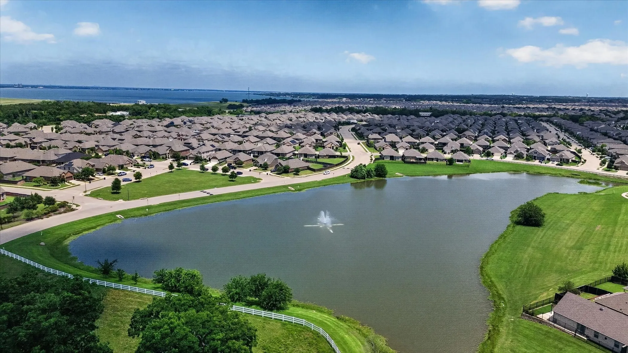Community featuring a large water body with a fountain, surrounded by residential properties, and a distant expanse of water