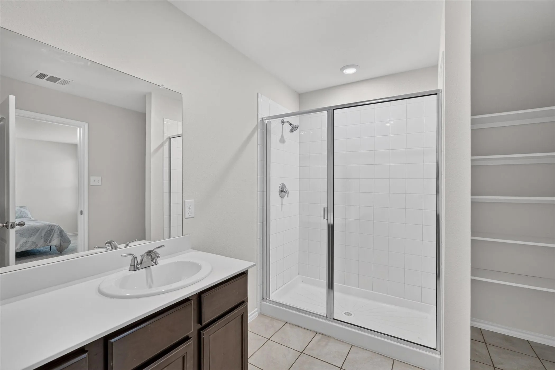 Spa-inspired primary bathroom featuring a dual-sink vanity with dark wood cabinetry and white quartz countertop, framed mirror with integrated lighting, frameless glass shower enclosure with subway tile surround, chrome fixtures, recessed ceiling lighting, and tile flooring throughout