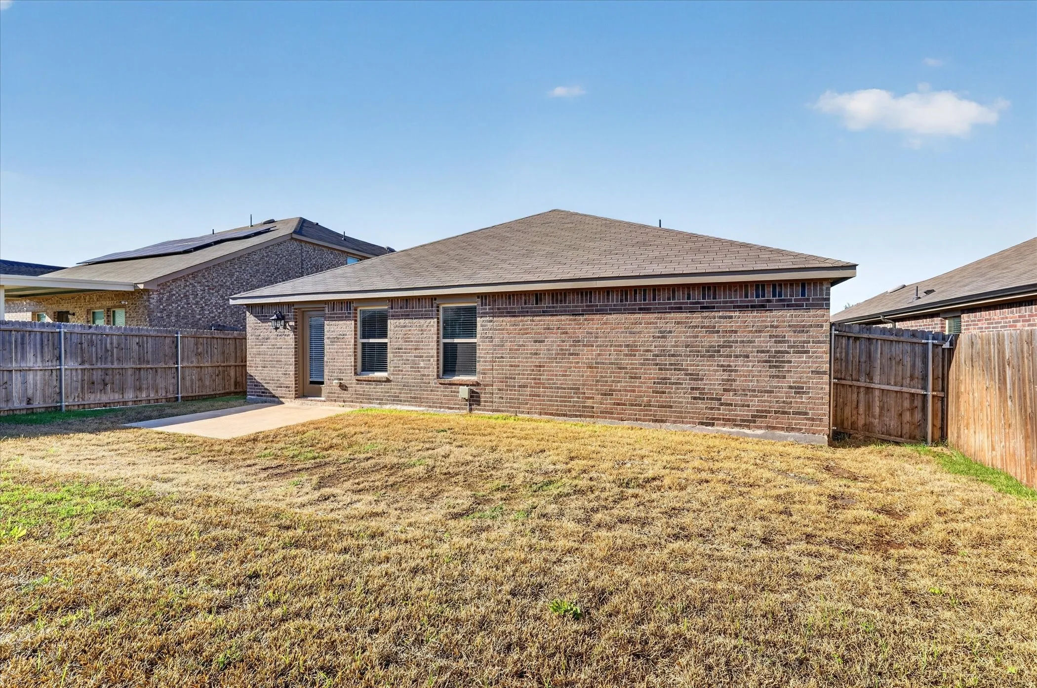 Brick exterior with multiple windows, leading to a concrete patio