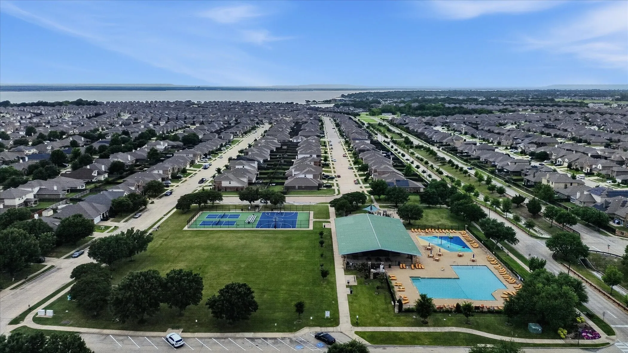 Aerial view showcasing a master-planned community with tree-lined streets, manicured green spaces, and resort-style amenities including multiple swimming pools and recreational facilities