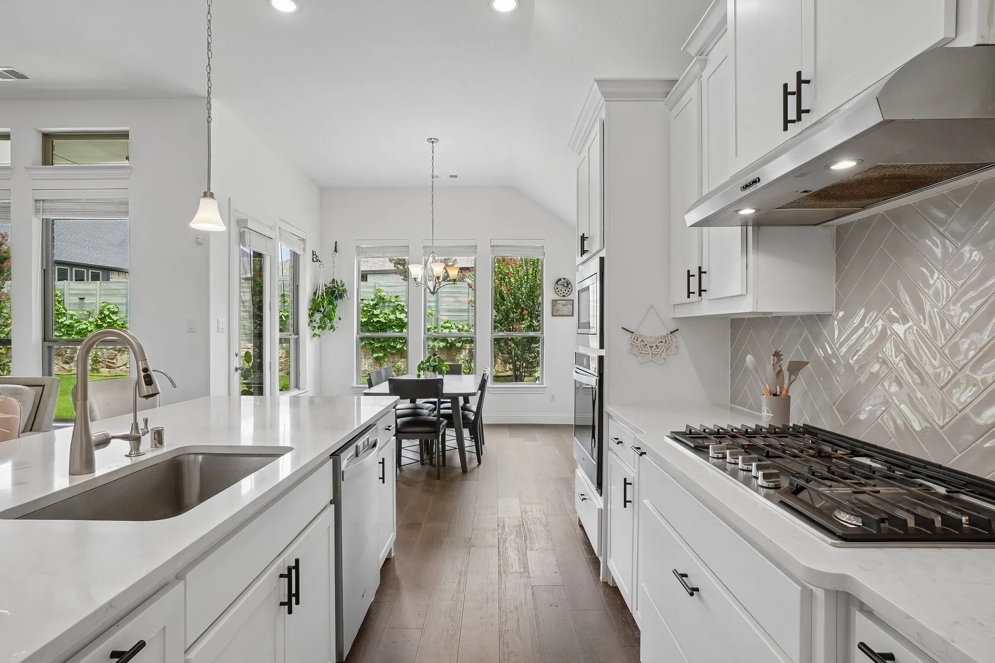 White shaker cabinetry, light-toned countertops, stainless steel sink with a gooseneck faucet, integrated dishwasher, and a herringbone-patterned tile backsplash