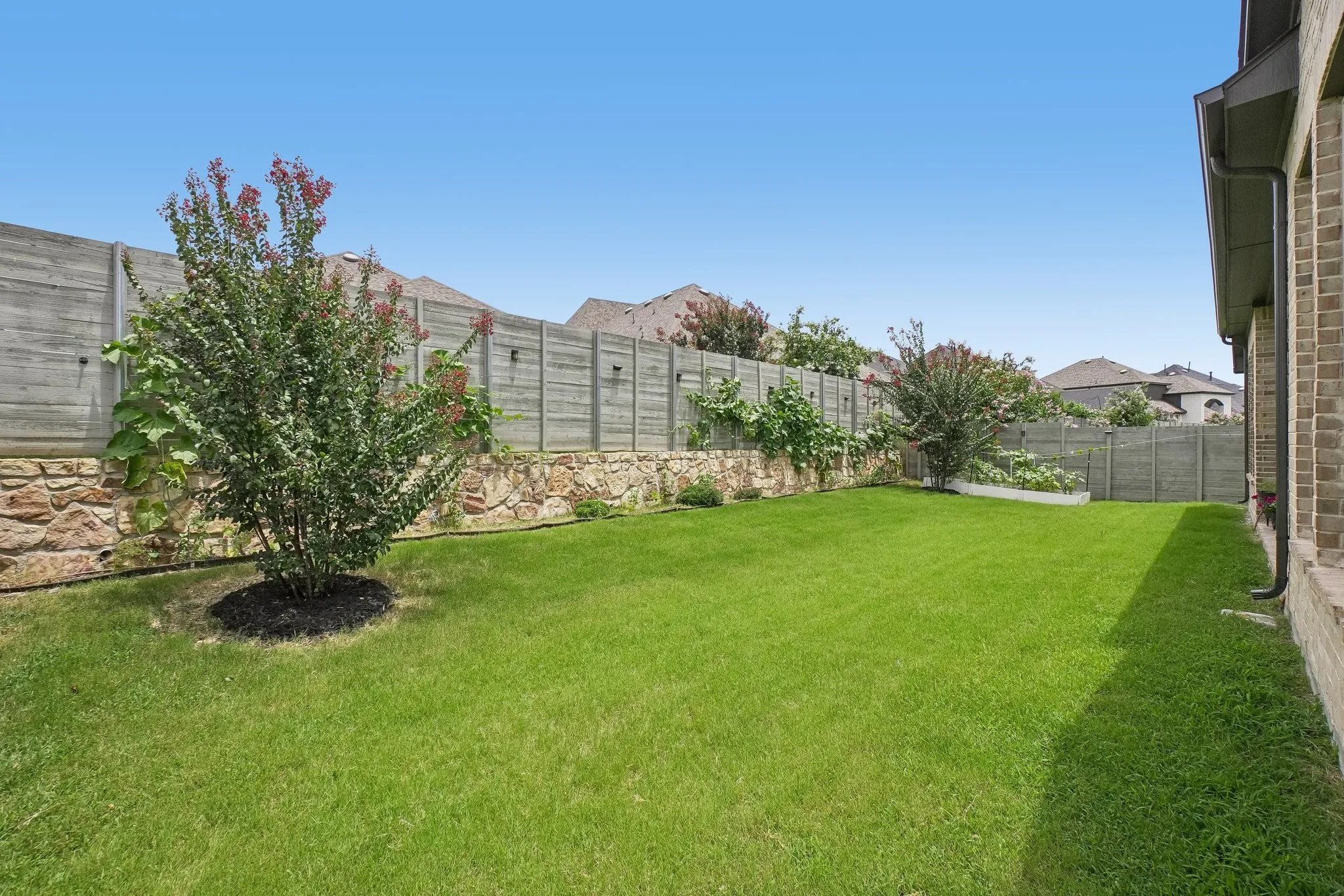 Expansive backyard featuring a manicured lawn, stone retaining wall, and mature landscaping