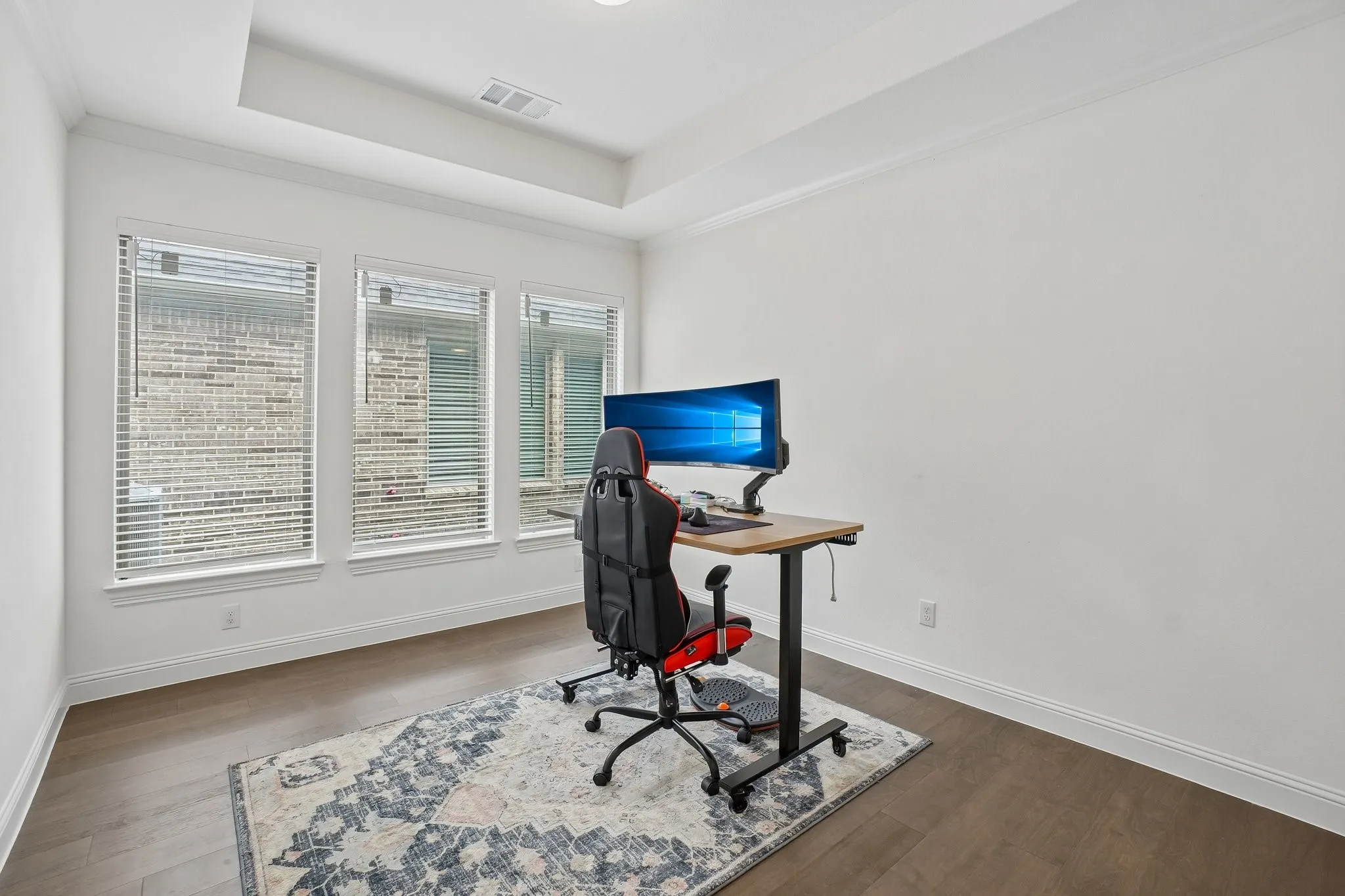 Wood-finish flooring with white baseboards, a tray ceiling, and three windows featuring blinds