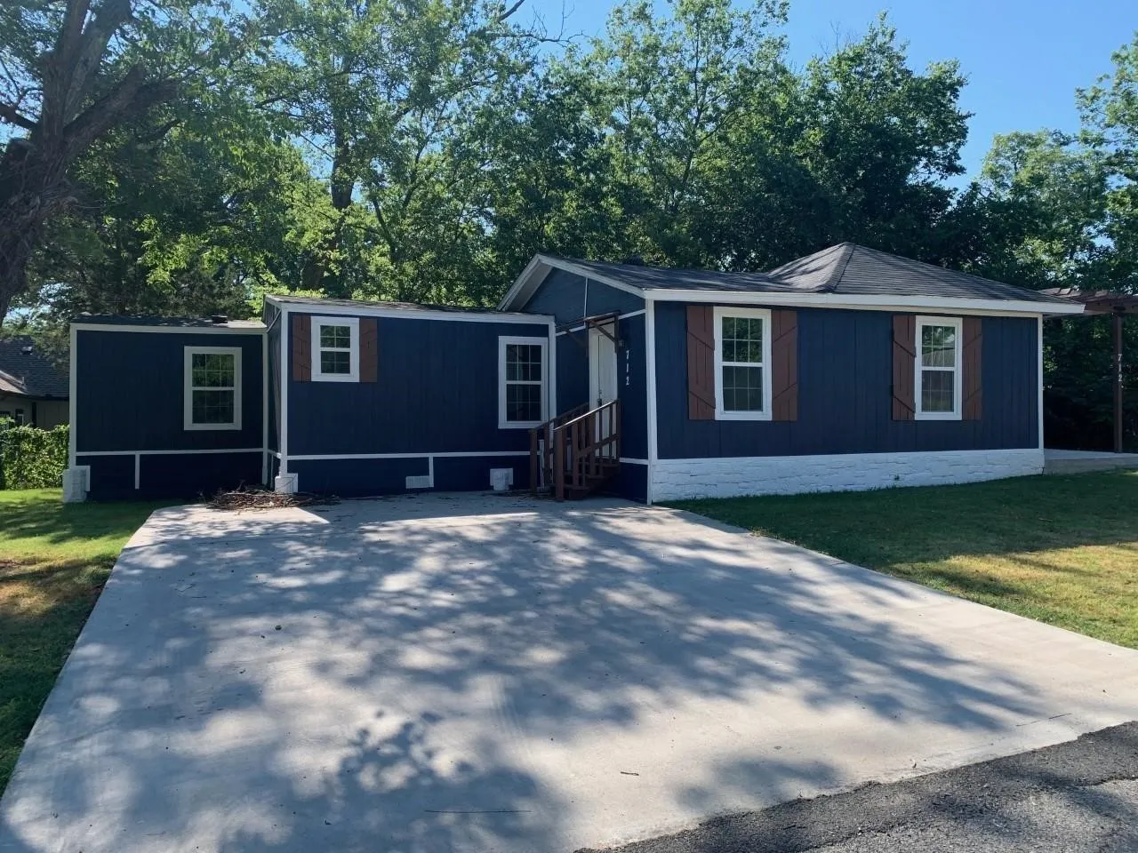 Blue exterior siding with white trim, brown wood-finish shutters, white-framed windows, and a paved driveway