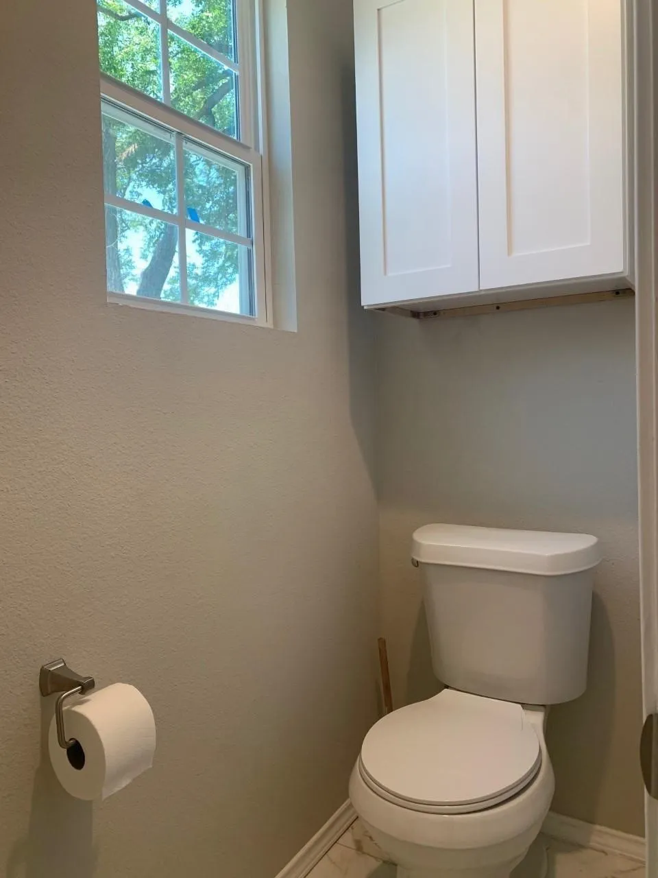 White shaker-style overhead cabinetry, a white toilet fixture, and a window with grid detailing
