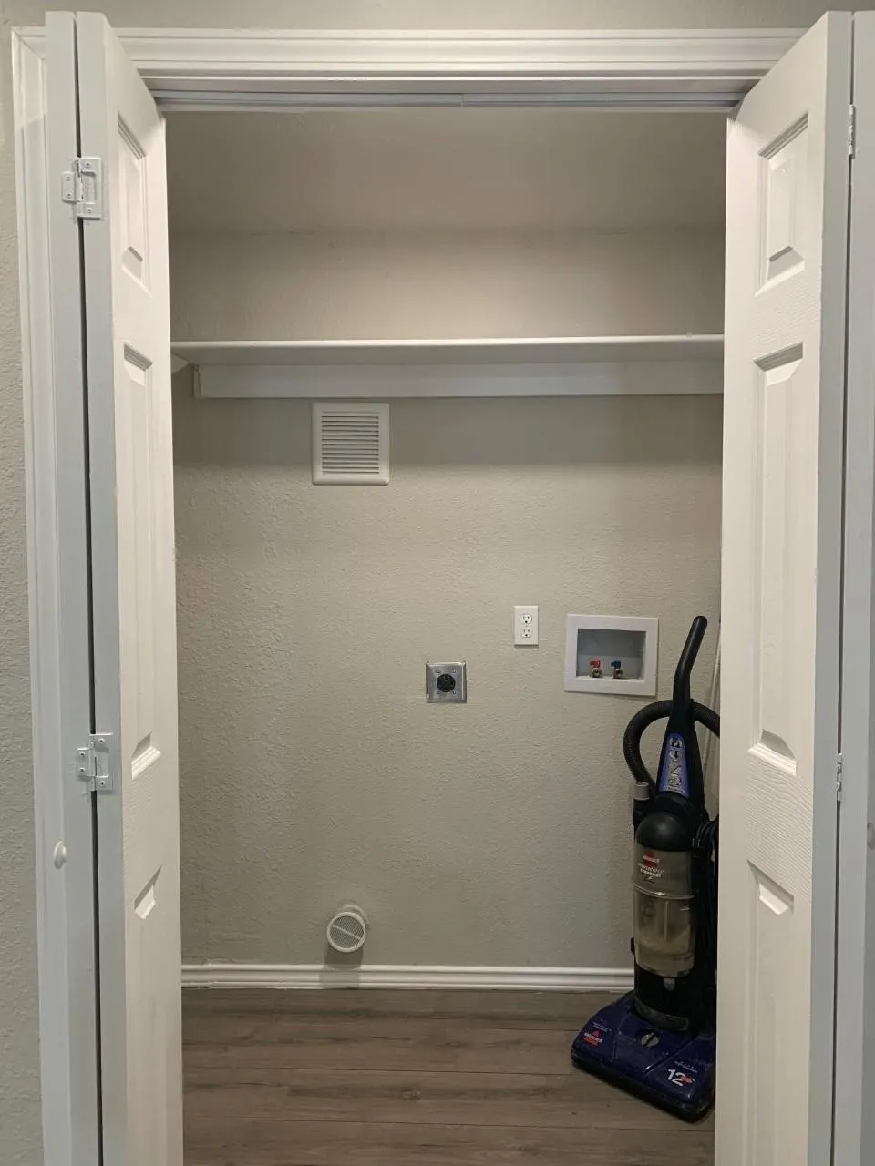 Laundry closet with wood-finish flooring, bi-fold doors, water hookups, and a wall shelf