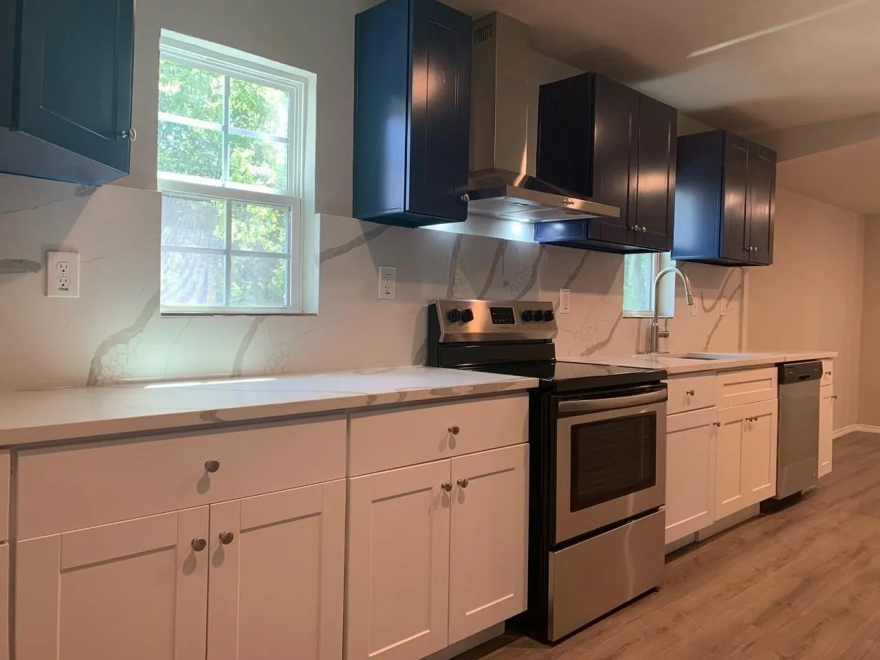 Contemporary kitchen featuring two-tone cabinetry, stainless steel appliances, a stainless steel range hood, quartz countertops, and wood-finish flooring