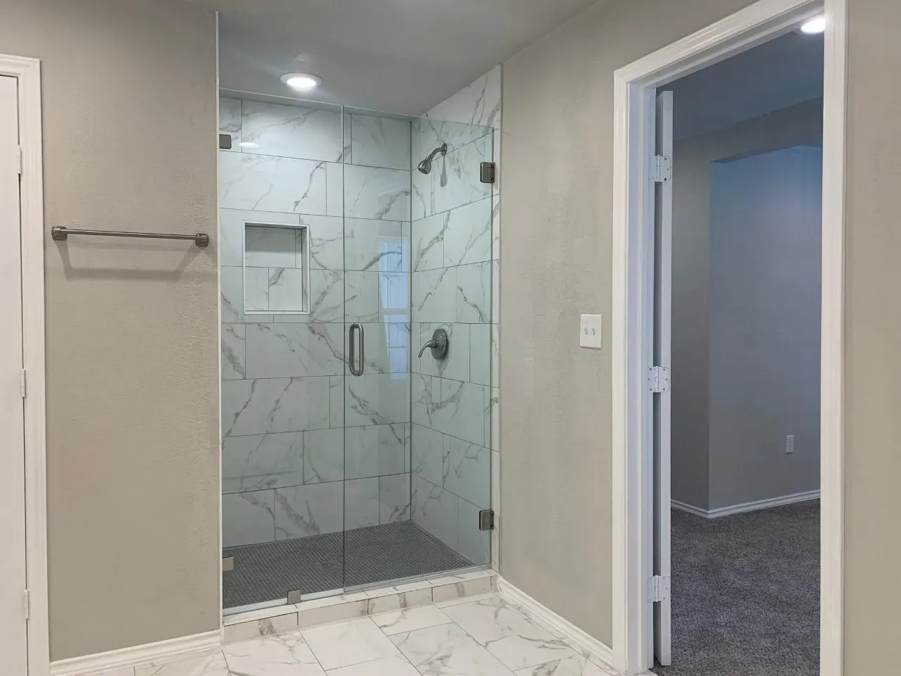 Glass-enclosed shower with a tiled interior, recessed shower niche, and a dark-finish shower head and controls