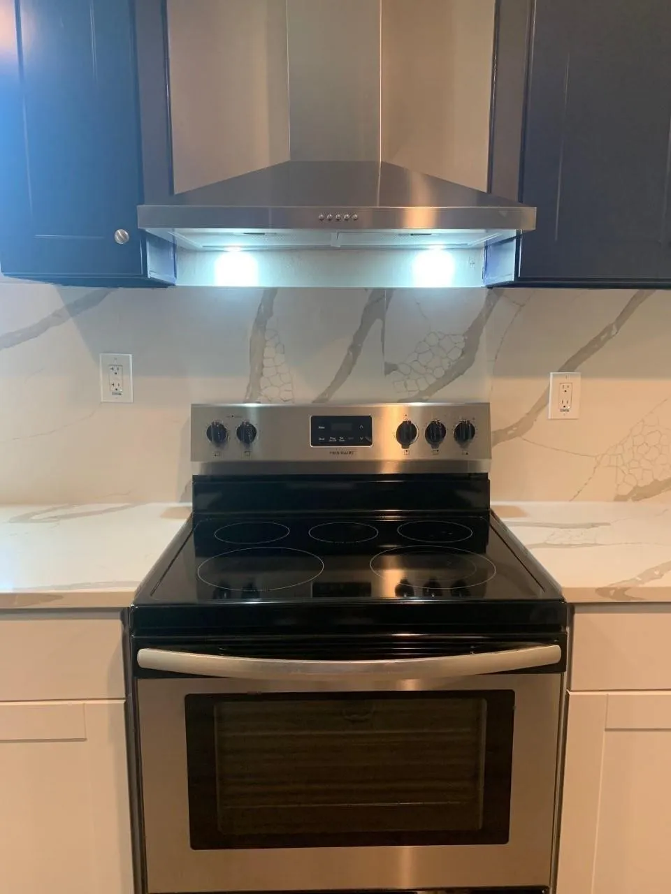 Stainless steel range with a smooth cooktop, stainless steel range hood, white countertops, and white and dark-colored cabinetry
