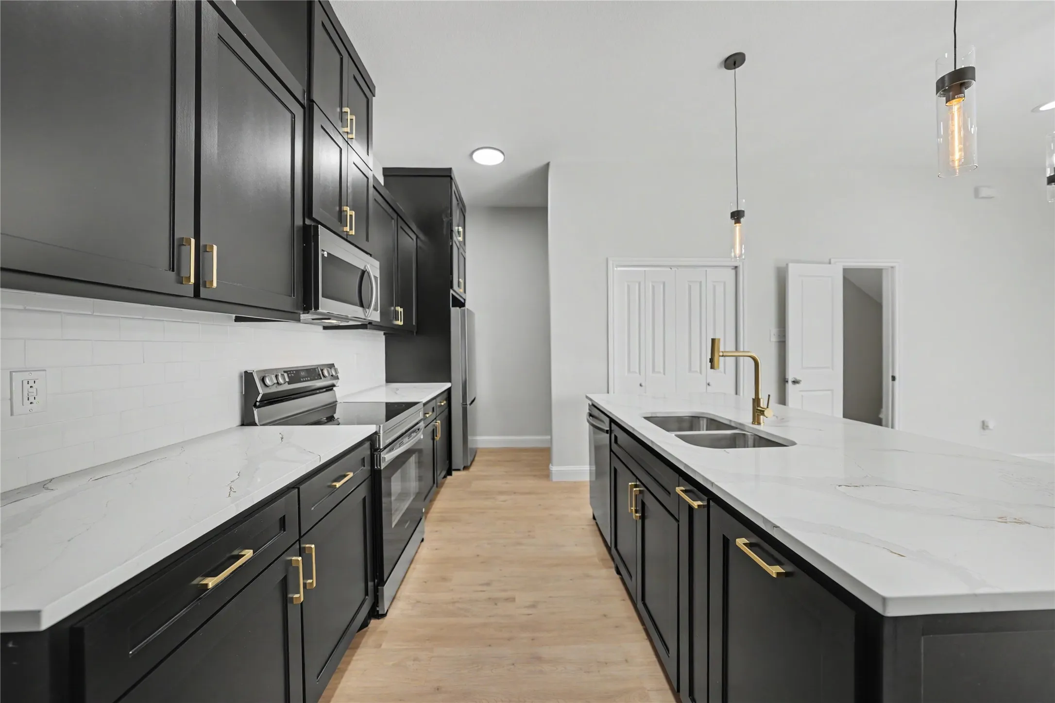Kitchen featuring black cabinetry, stainless steel appliances, white subway tile backsplash, white countertops, and wood-finish flooring