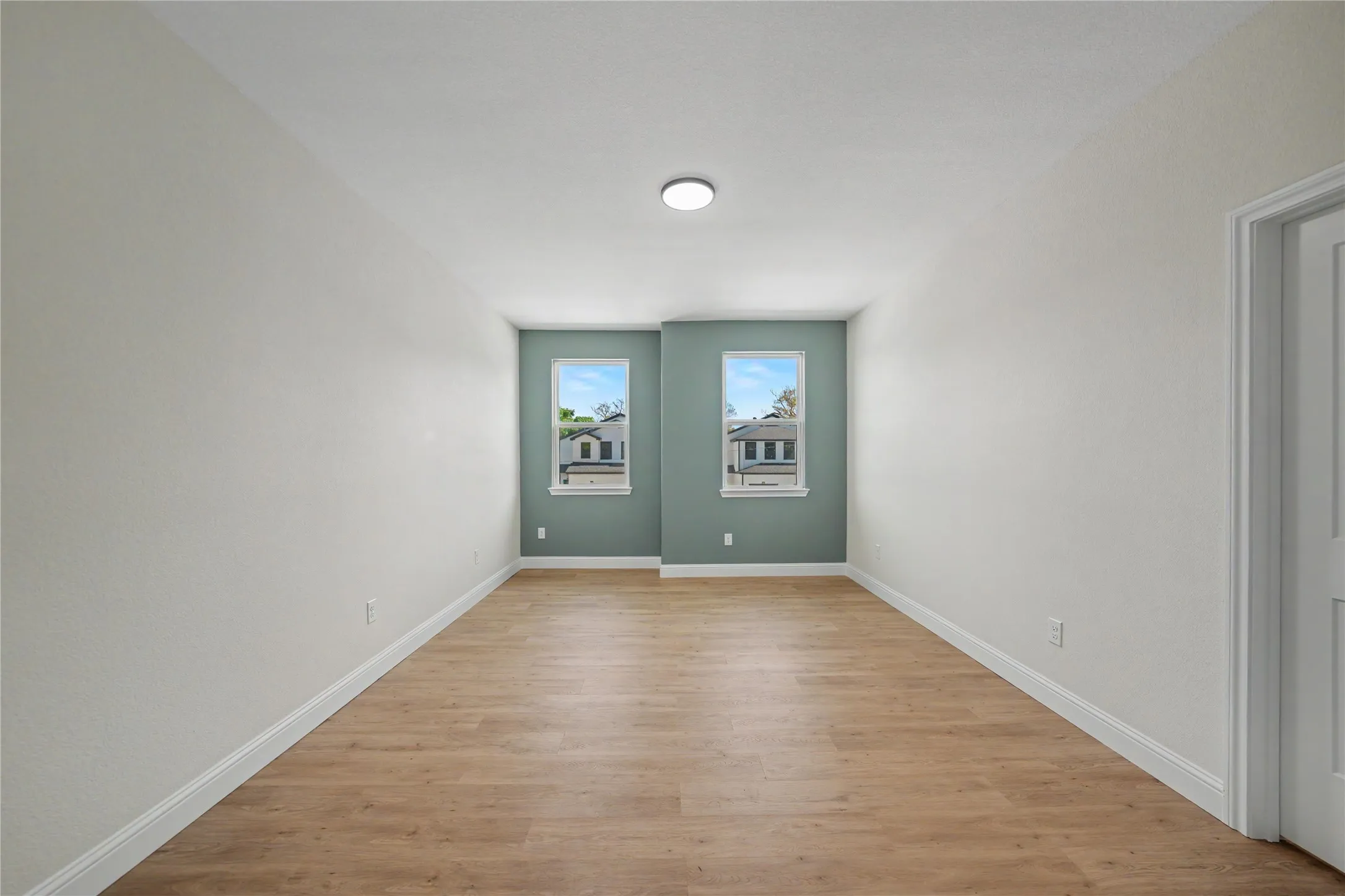 Upstairs bedroom featuring two windows with white trim, and wood-finish flooring