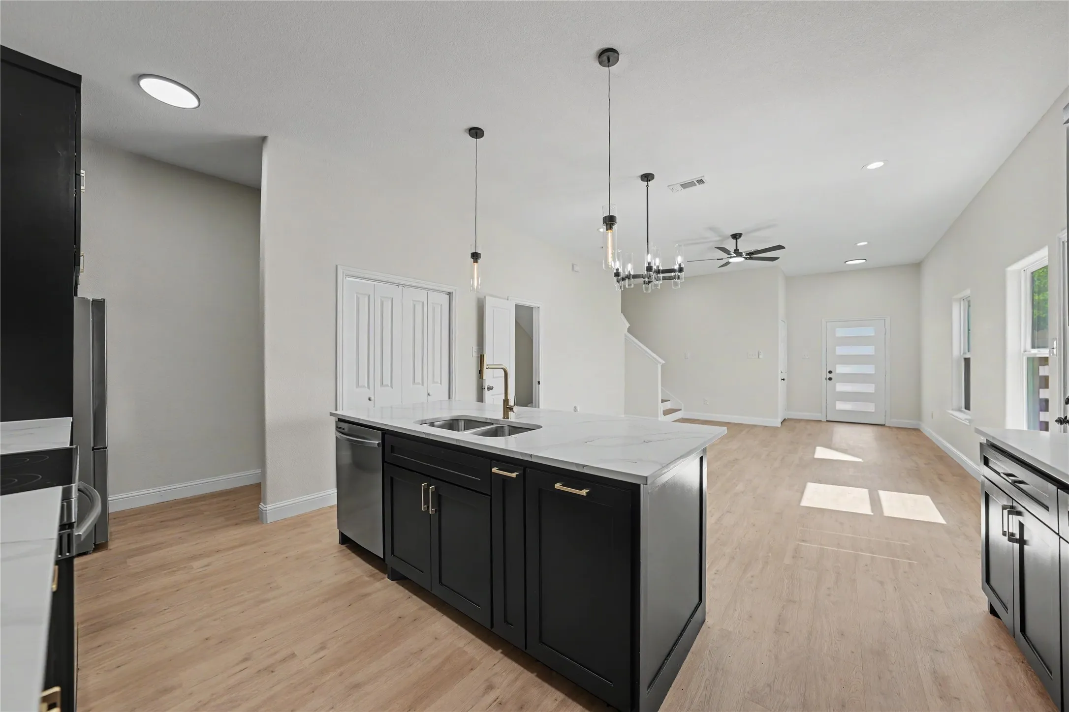Open-concept living space featuring wood-finish flooring, a kitchen island with stone countertops, a stainless steel dishwasher, and a contemporary chandelier