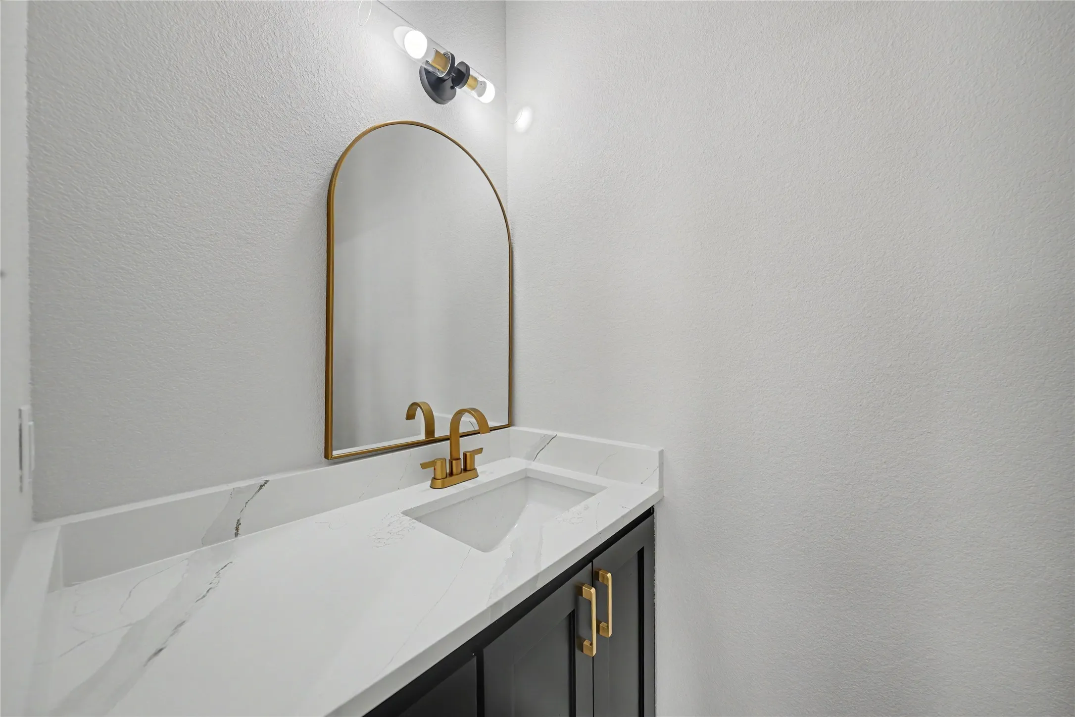 Half Bath Downstairs featuring a modern vanity with an integrated sink, white countertop with veining, matte black base cabinetry, and gold-finish hardware