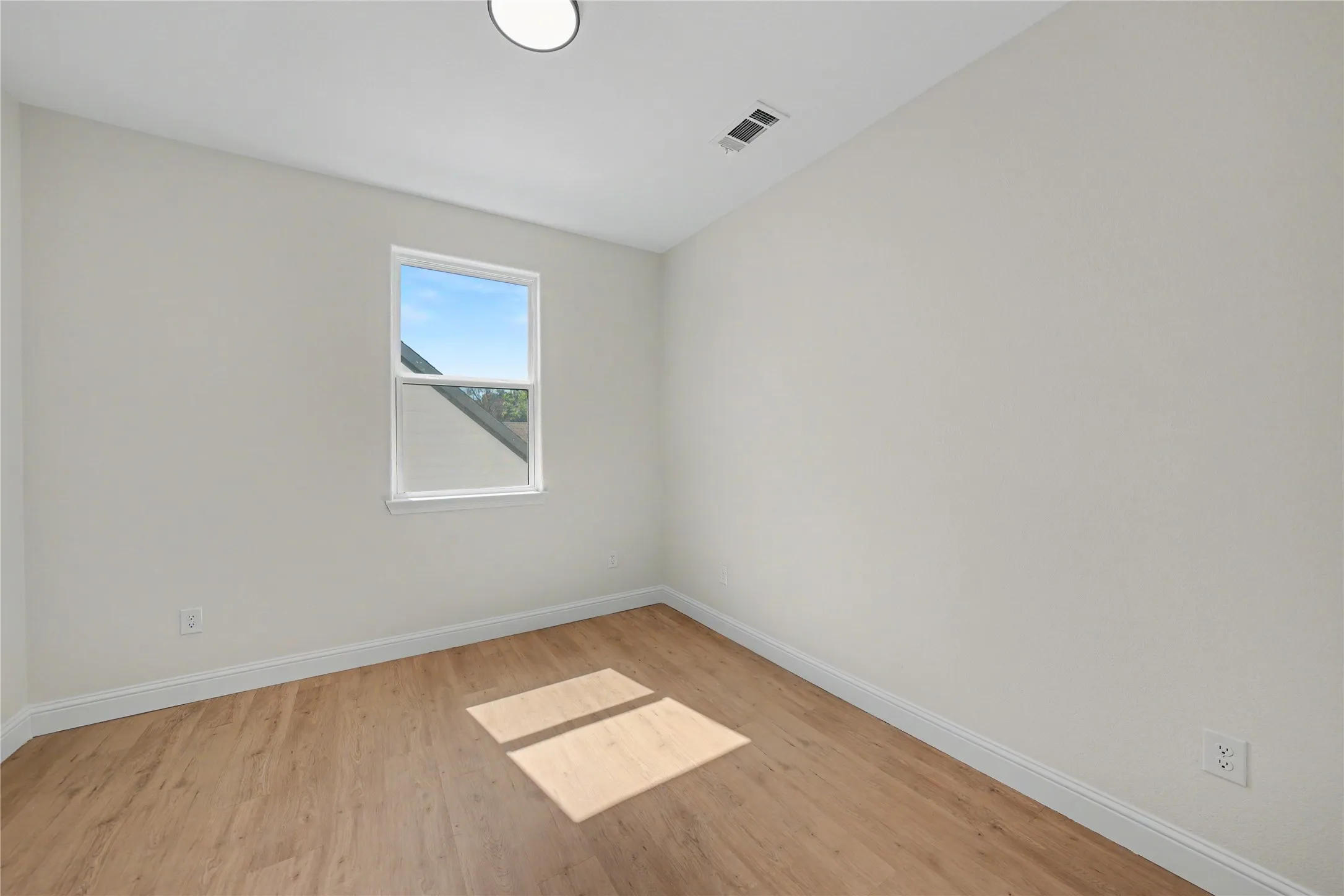 Upstairs bedroom featuring wood-finish flooring, white walls, and a single window with a white frame