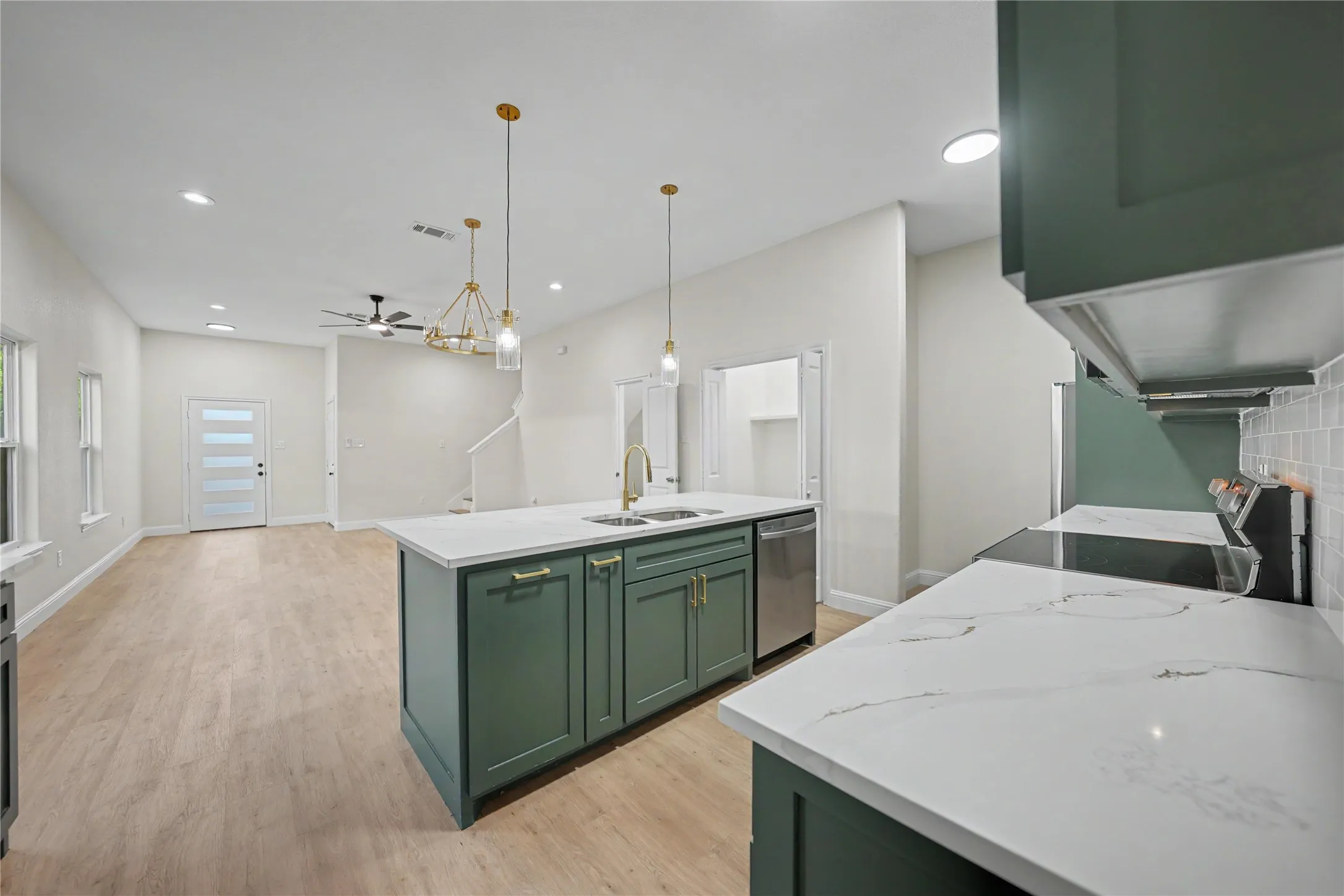 Kitchen island with green cabinetry and white countertops, featuring pendant lighting and a stainless steel dishwasher