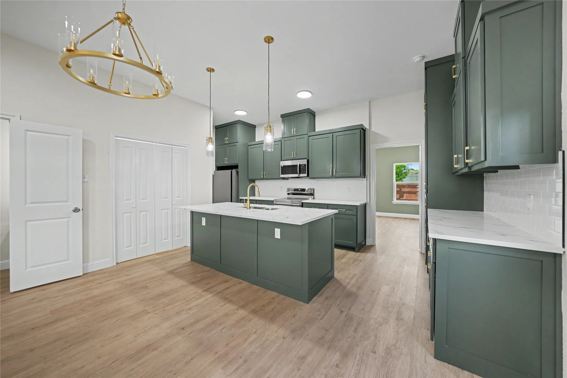 Contemporary kitchen featuring custom green cabinetry, a central island with countertop, stainless steel appliances, and wood-finish flooring