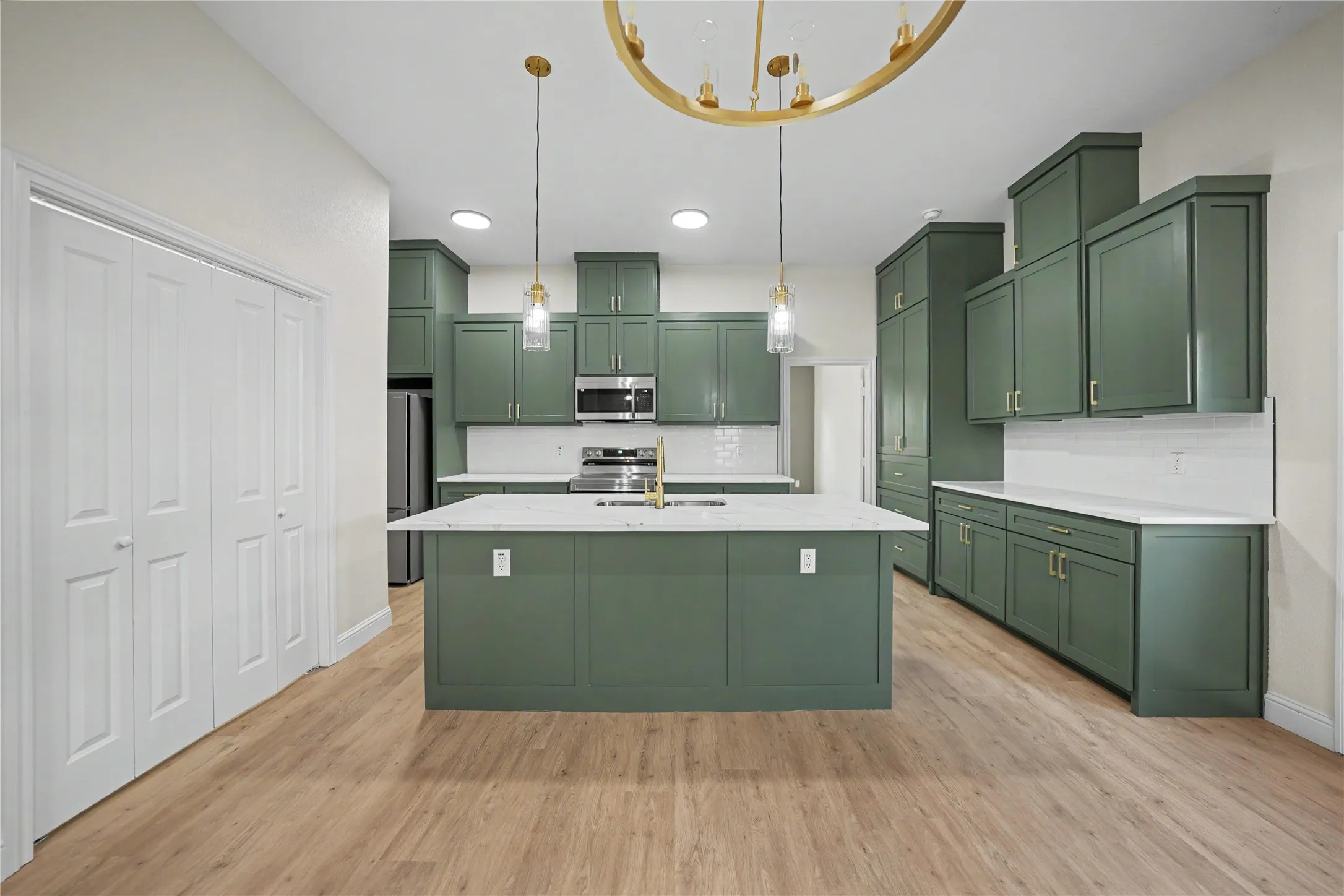 Kitchen featuring dark green cabinetry, white countertops, stainless steel appliances, wood-finish flooring, and a central island with pendant lighting