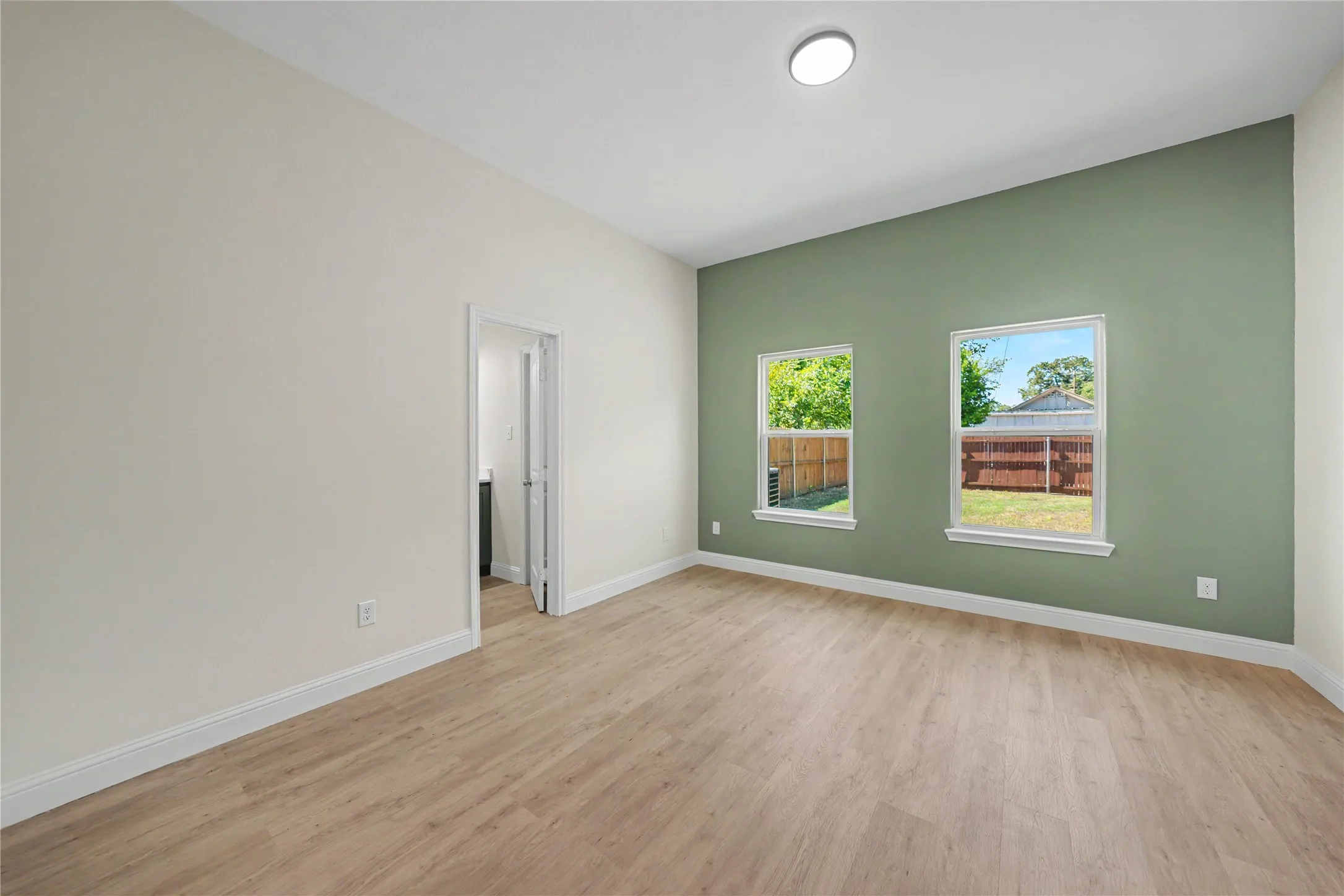 Bright room featuring light wood-finish flooring, a contemporary flush mount ceiling light, and two large windows
