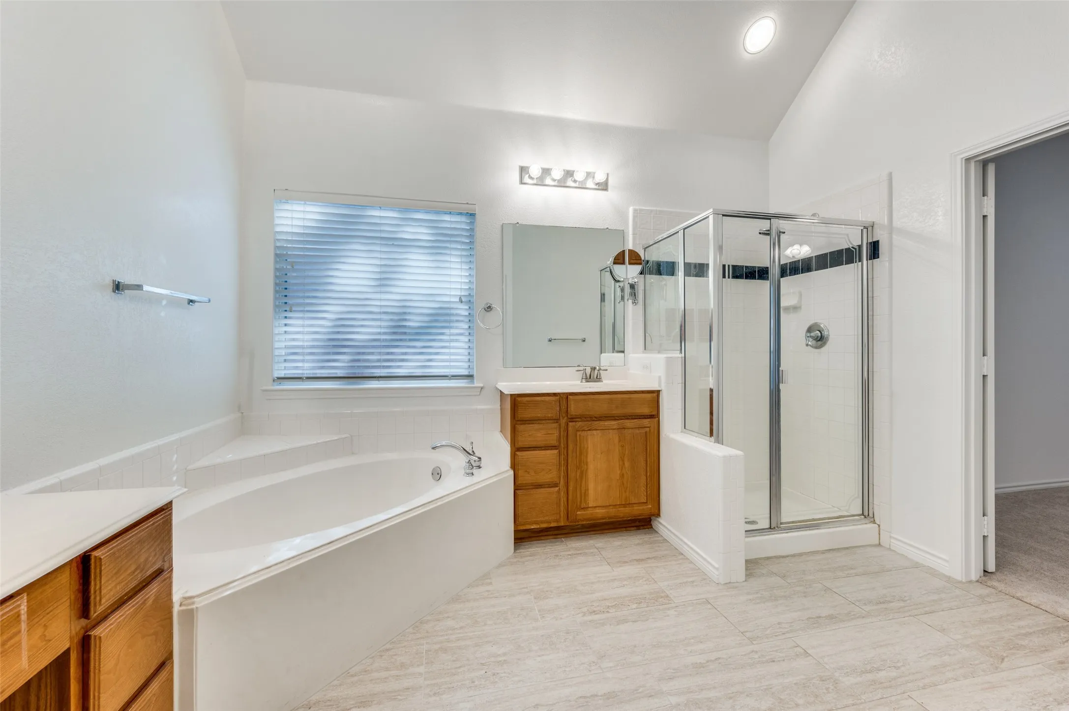 Spacious bathroom featuring a built-in soaking tub, separate glass-enclosed shower, a vanity with wood-finish cabinetry, and tiled flooring