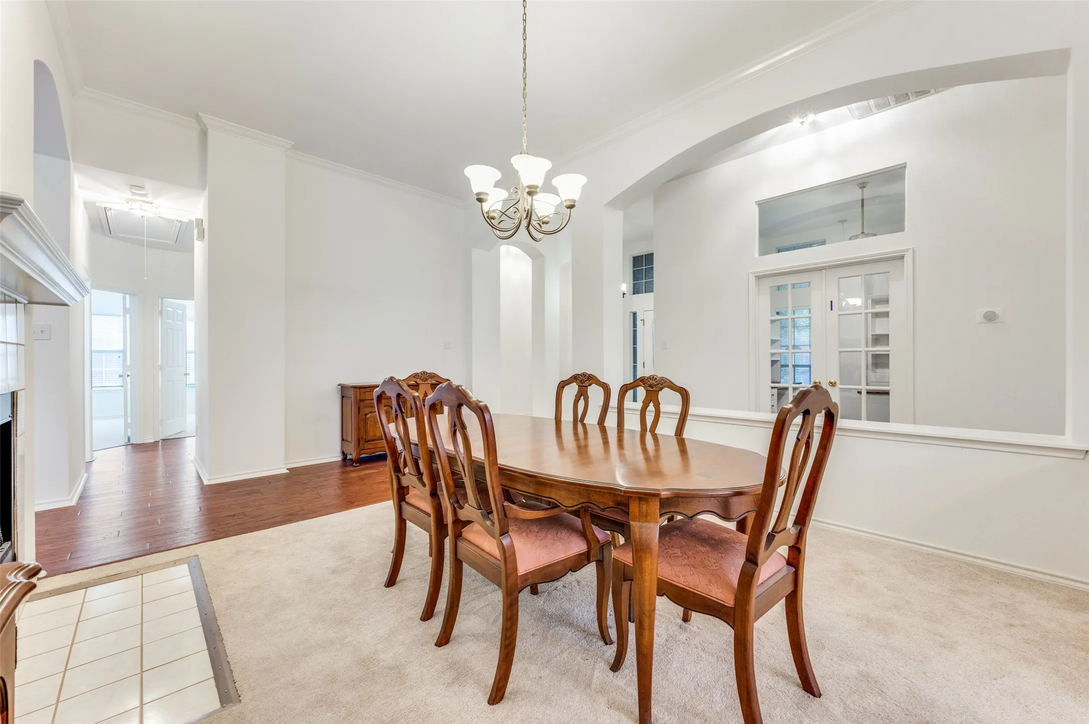 Carpeted dining area with a chandelier, featuring an arched entryway and French doors with an overhead transom window.  This can actually be utilized as a sitting room since there is an adjacent dining room.