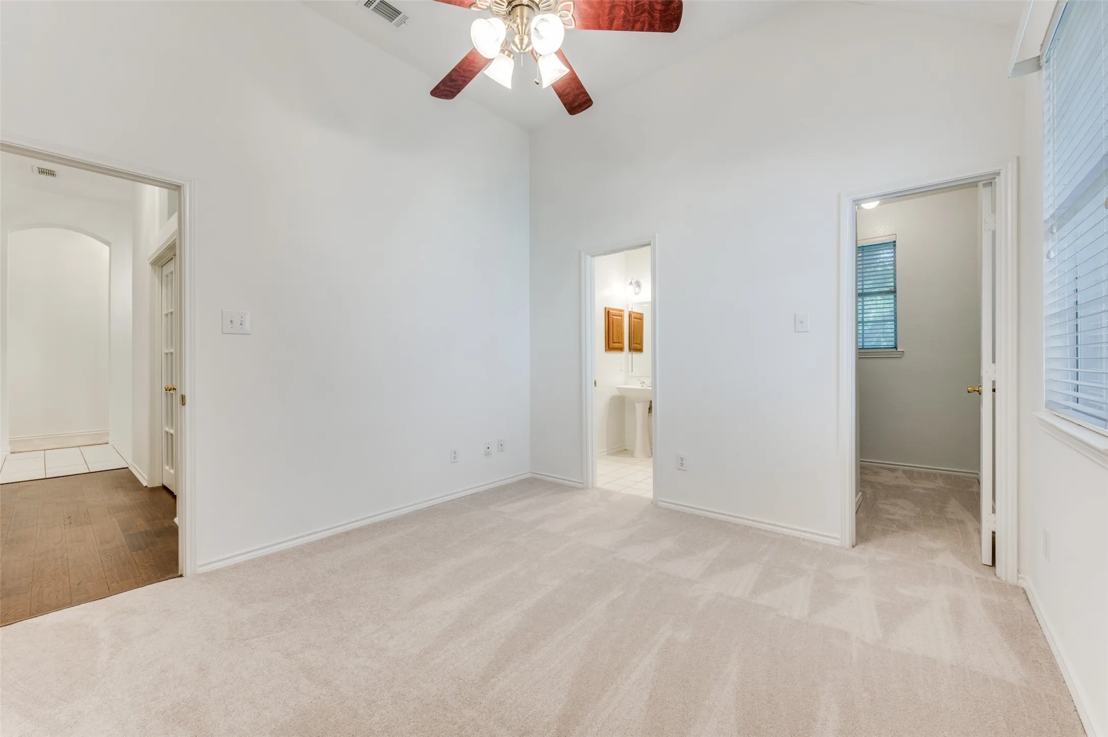 Vaulted ceiling, ceiling fan with light fixture, neutral wall color, plush carpet flooring, and a window with blinds