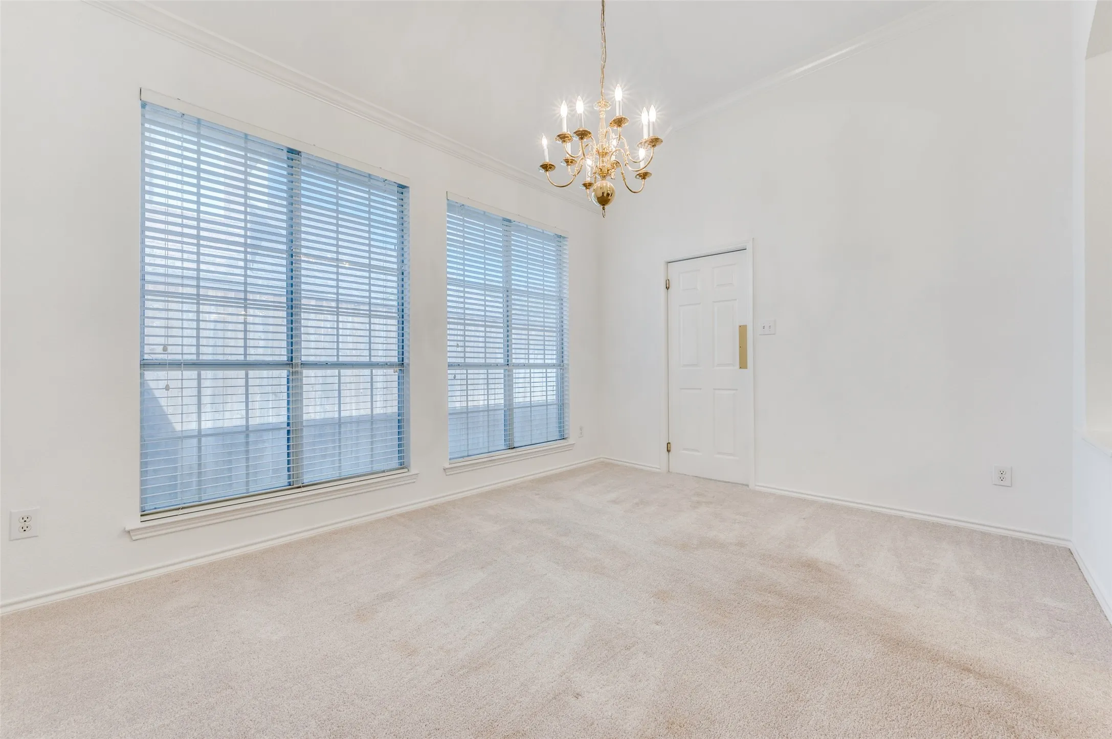 Vaulted ceiling featuring a brass chandelier, two large windows with horizontal blinds, neutral carpeting, and white trim